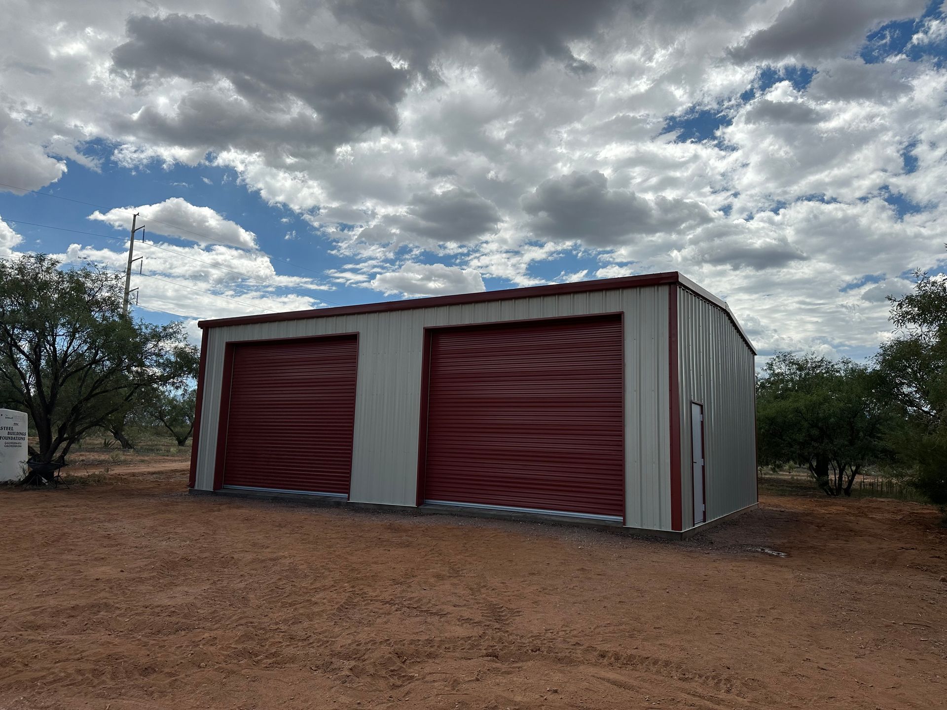 A metal building with two red garage doors in a dirt field.