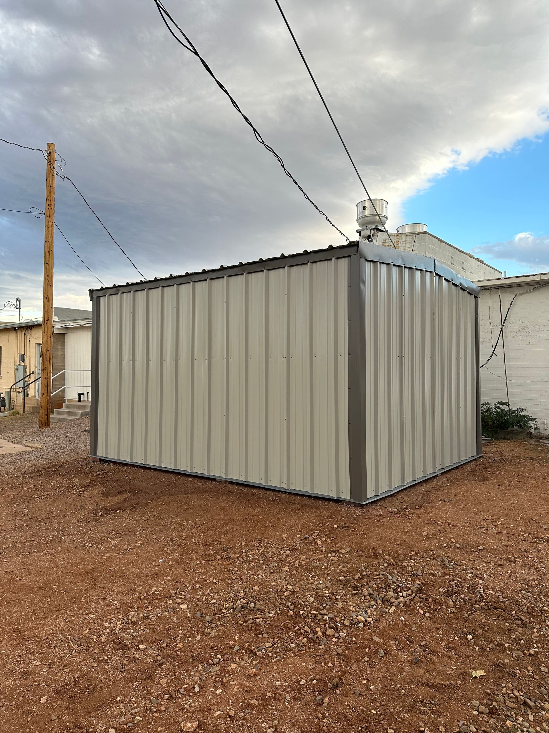A metal shed is sitting in the middle of a dirt field.