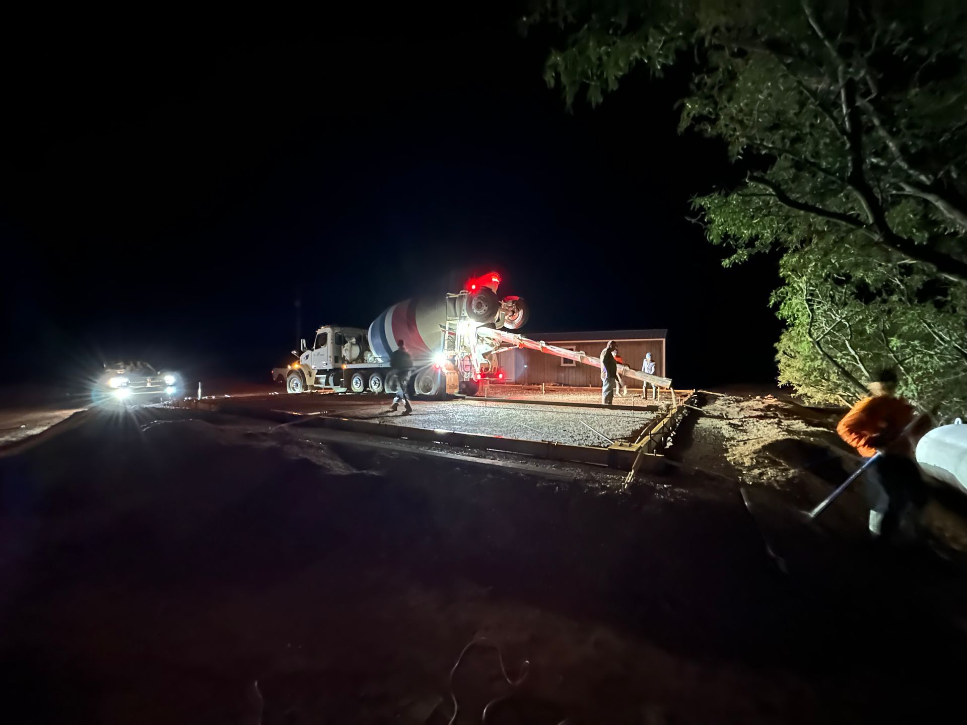 A concrete truck is pouring concrete on the side of a road at night.