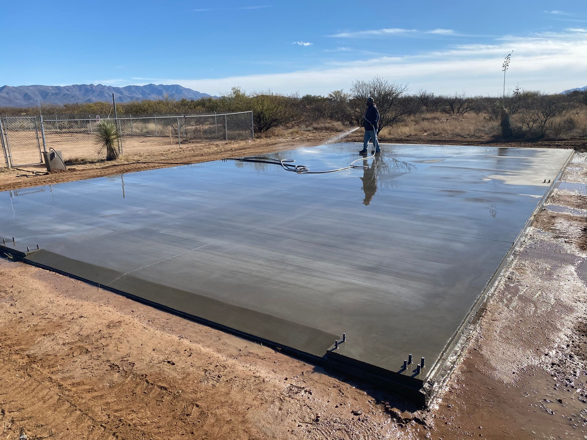 A man is spraying water on a concrete slab in the desert.