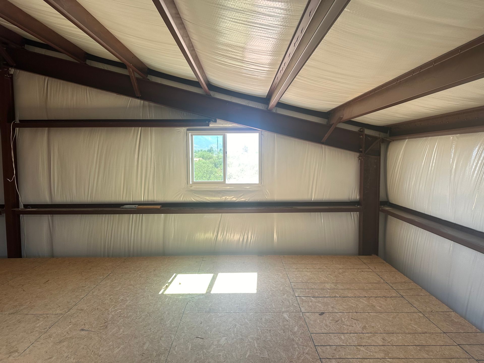 The inside of a metal building with a window and a wooden floor.