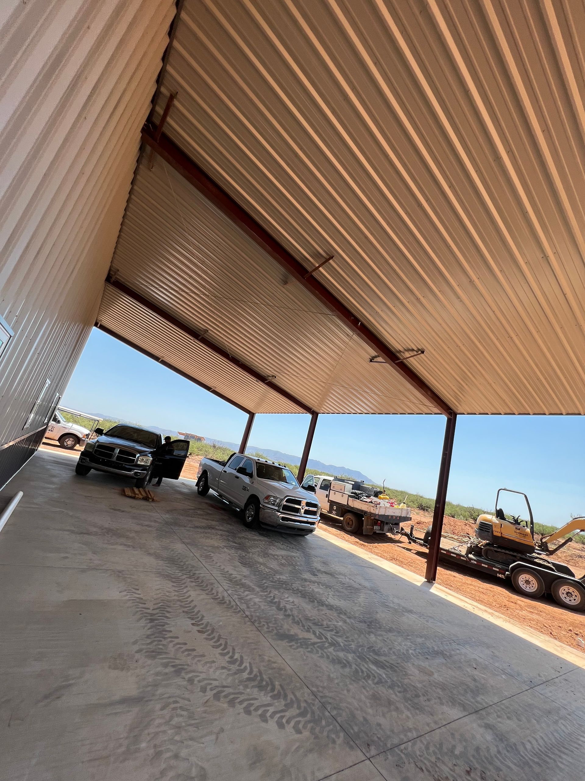 Two trucks are parked under a metal roof in a parking lot.