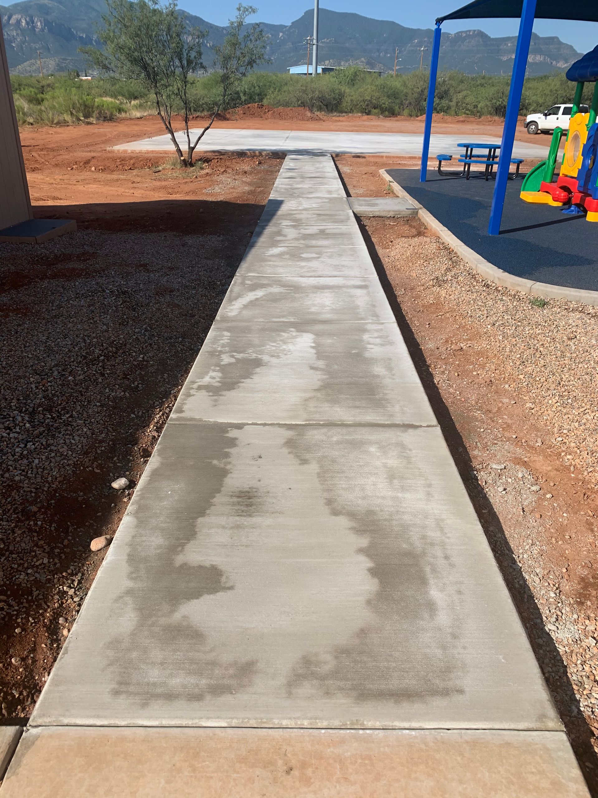 A concrete walkway leading to a playground with mountains in the background
