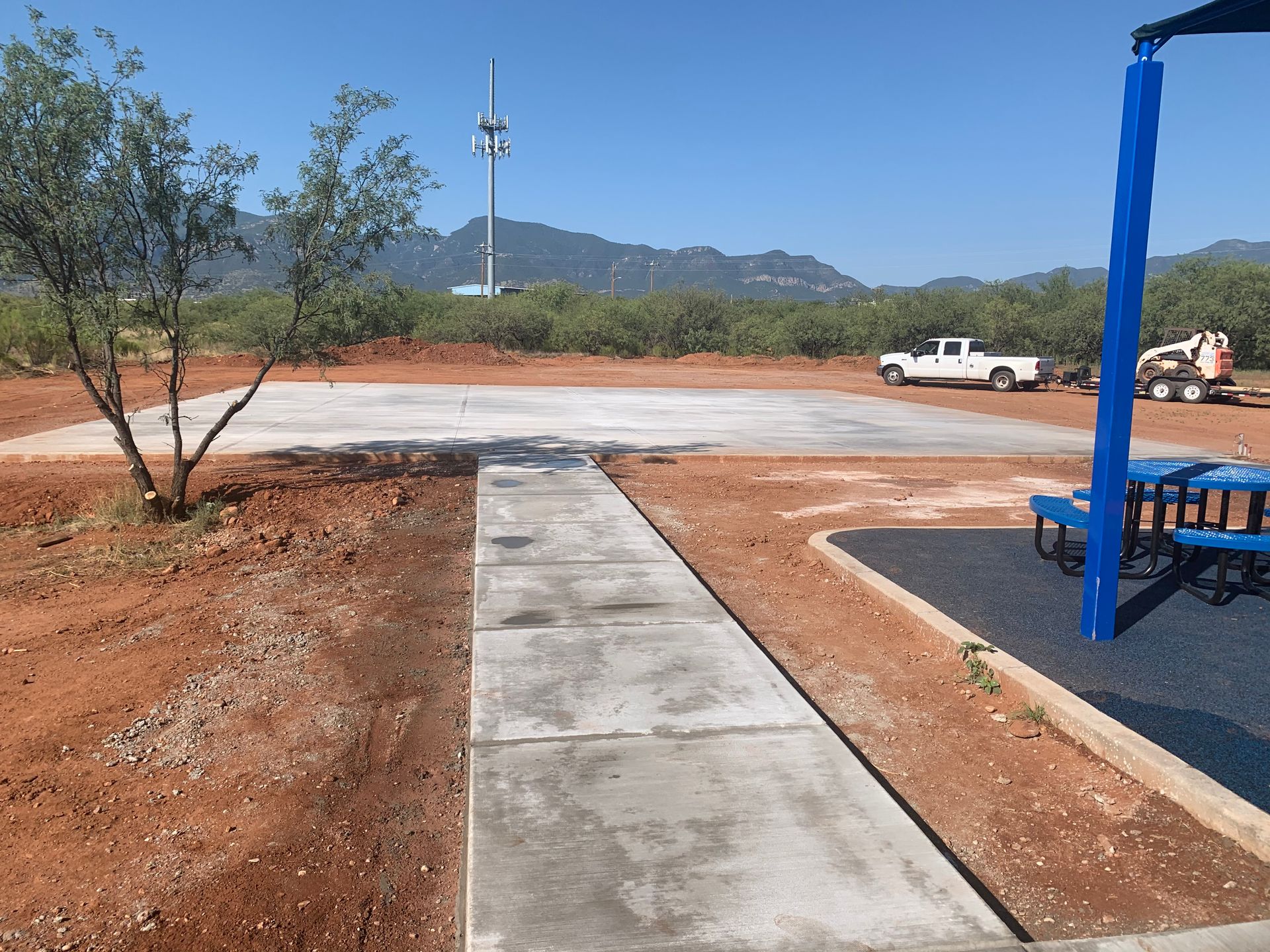 A concrete walkway leading to a picnic area with a blue umbrella.