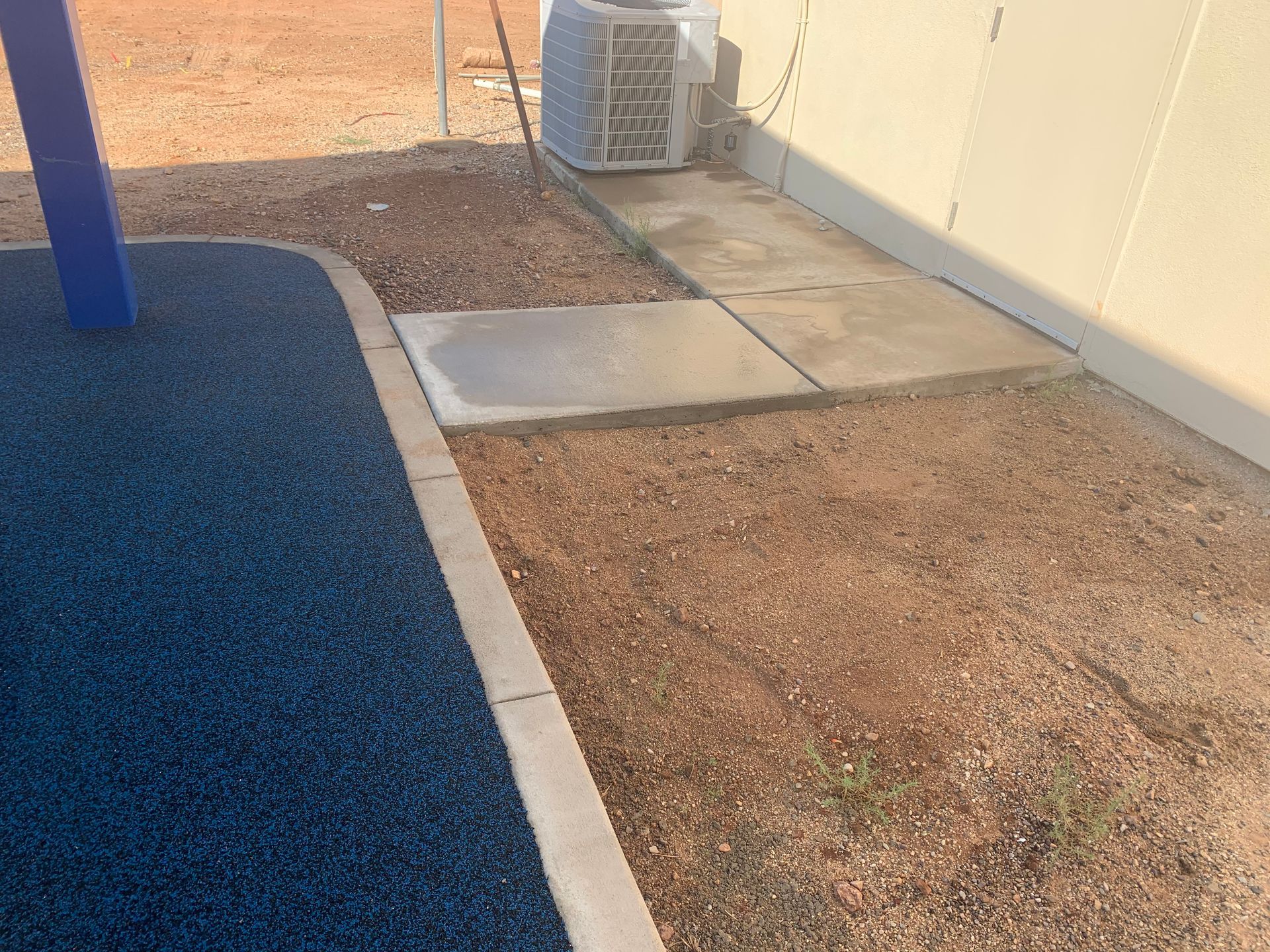 A sidewalk with a blue rubber border is next to a building.