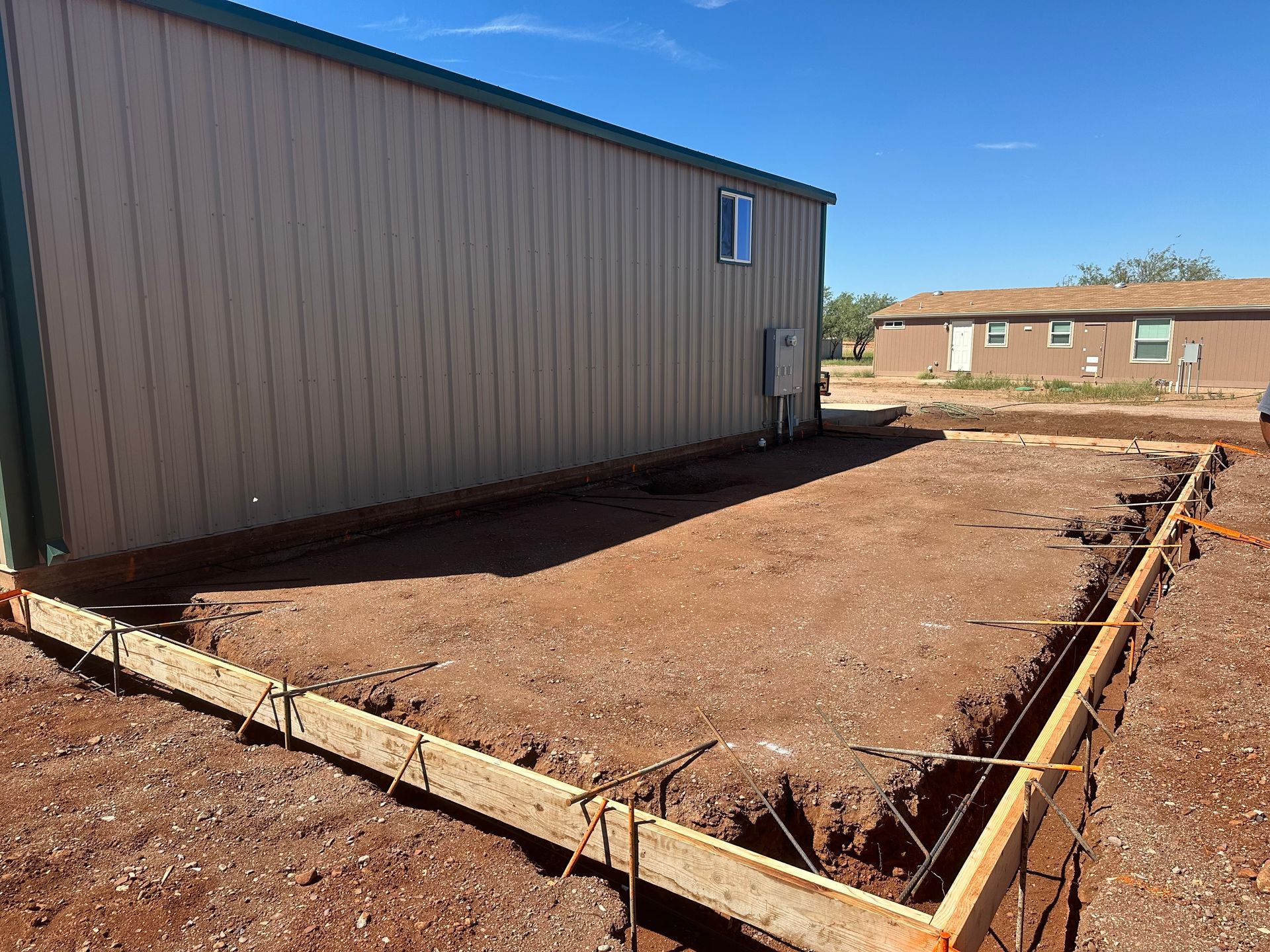 A large metal building is being built in a dirt field.