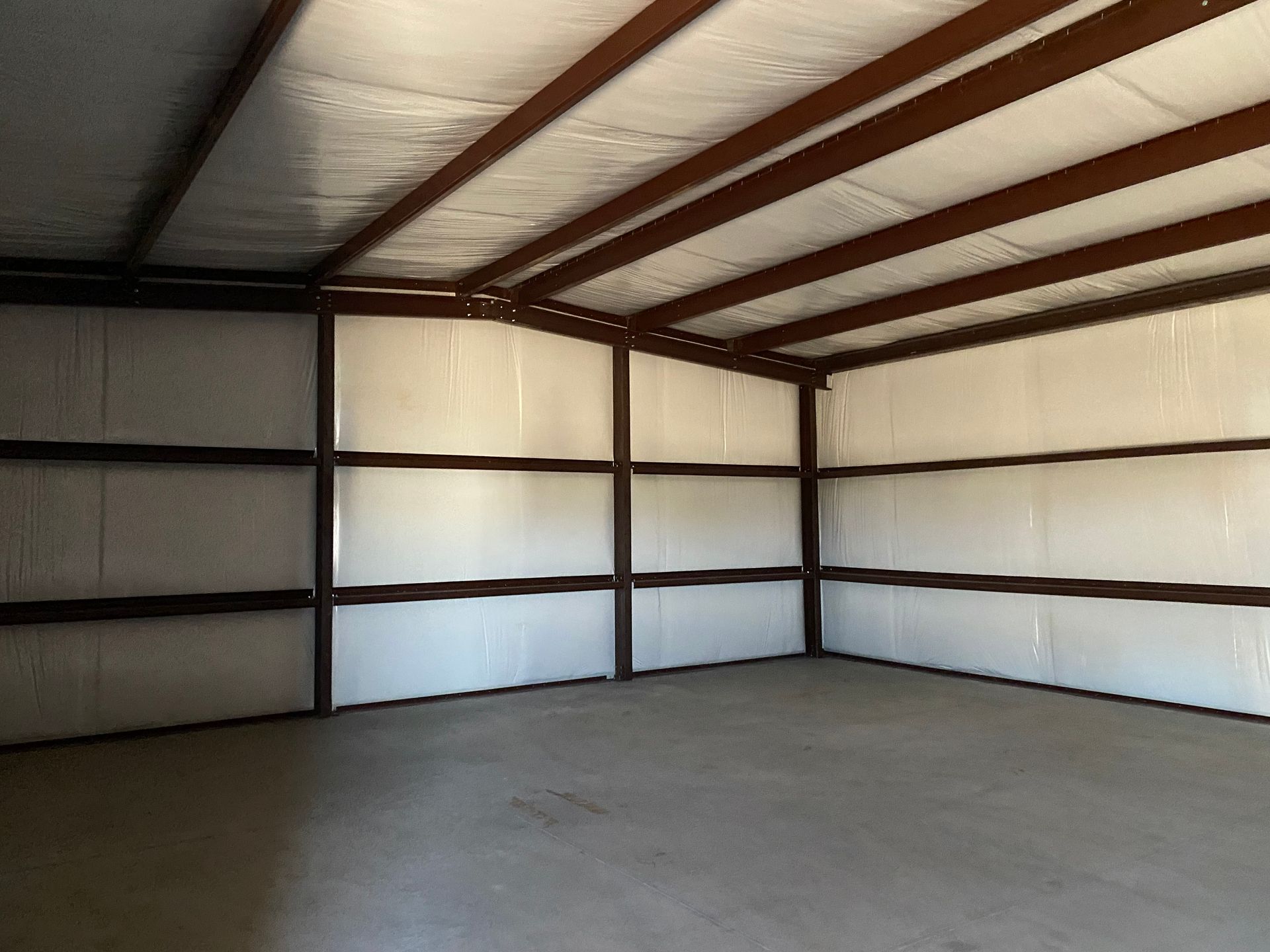 An empty metal building with white walls and brown beams