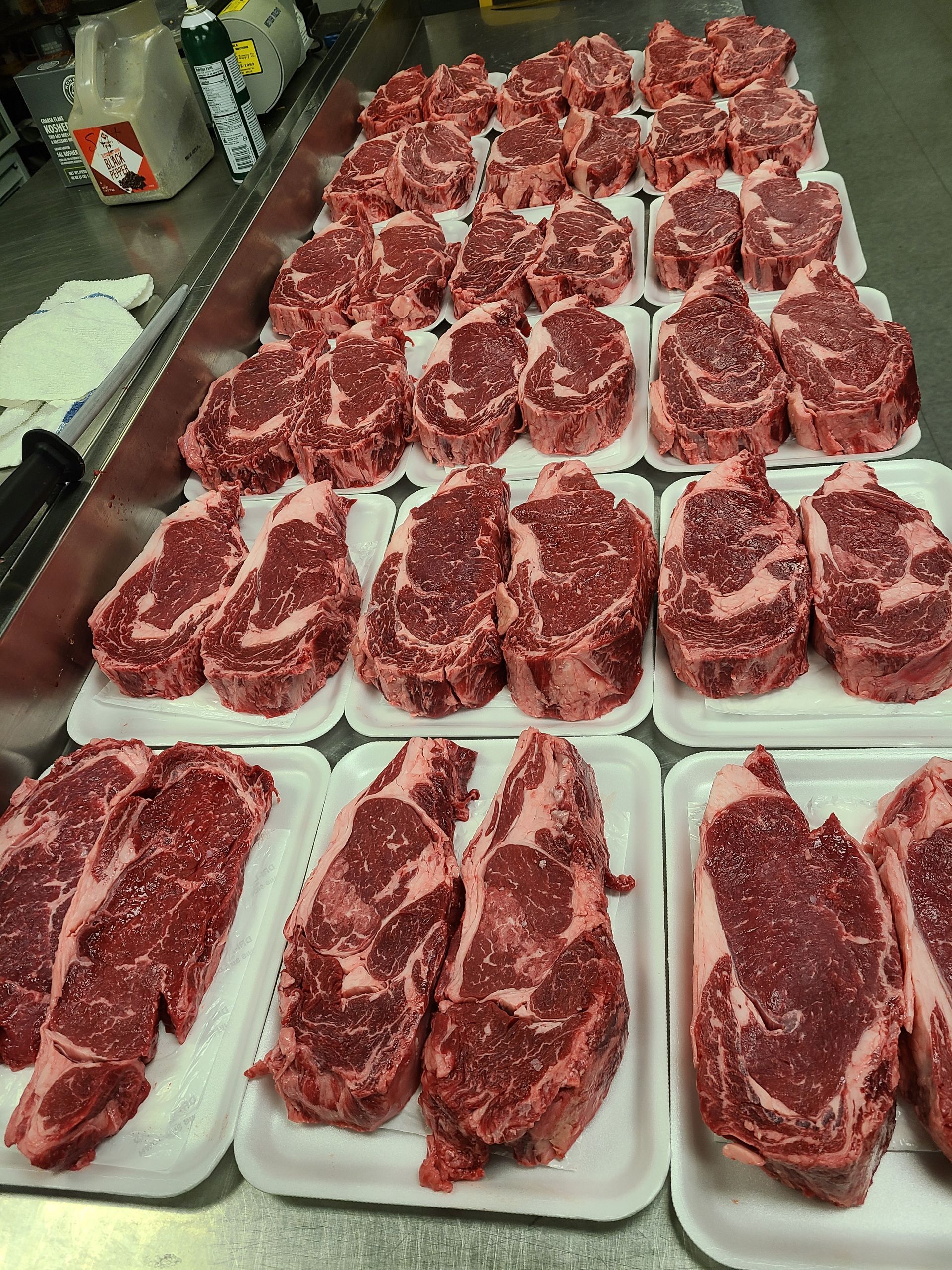 A bunch of steaks are sitting on styrofoam trays on a counter.