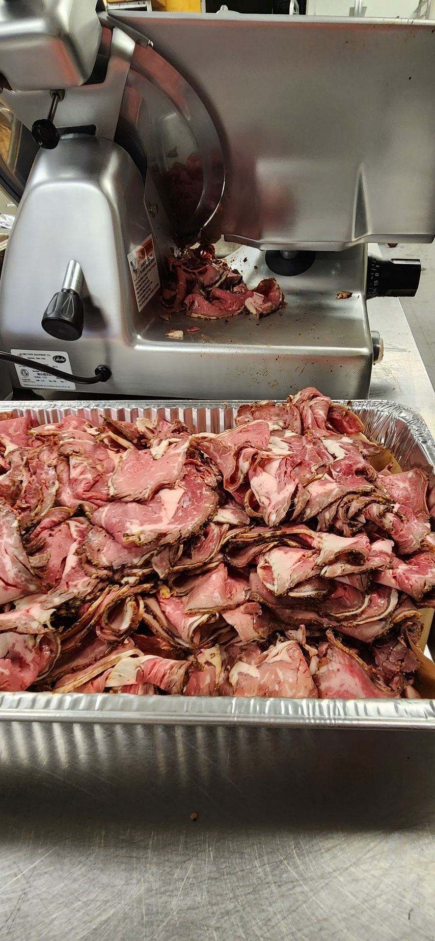 A tray of sliced roast beef next to a meat slicer.