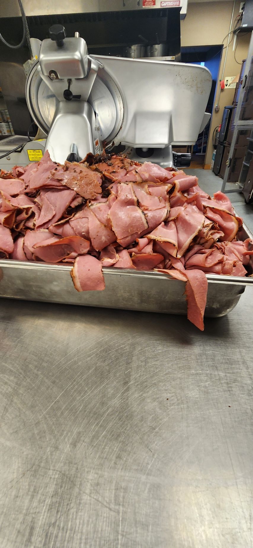 A tray of sliced meat is sitting on a counter next to a meat grinder.