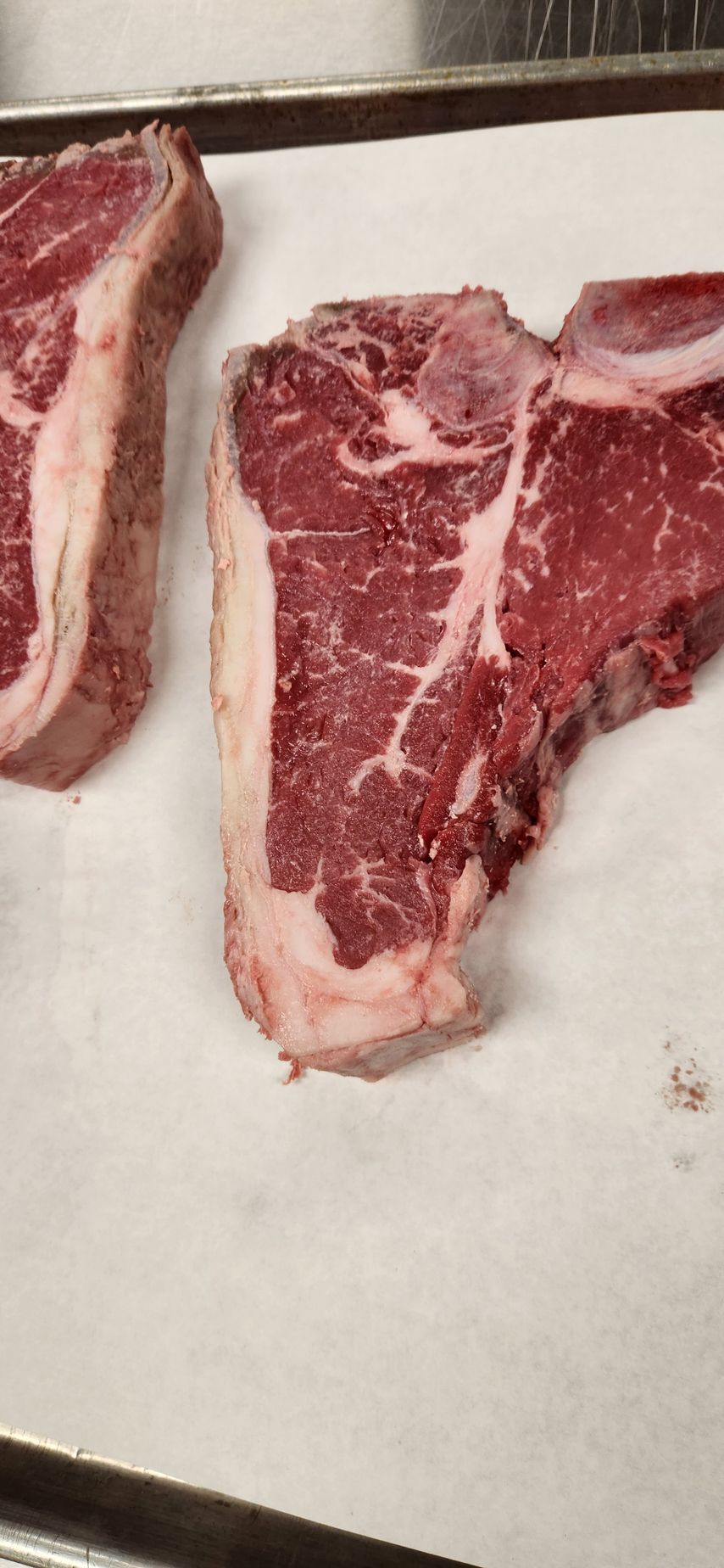 Two steaks are sitting on a piece of wax paper on a table.
