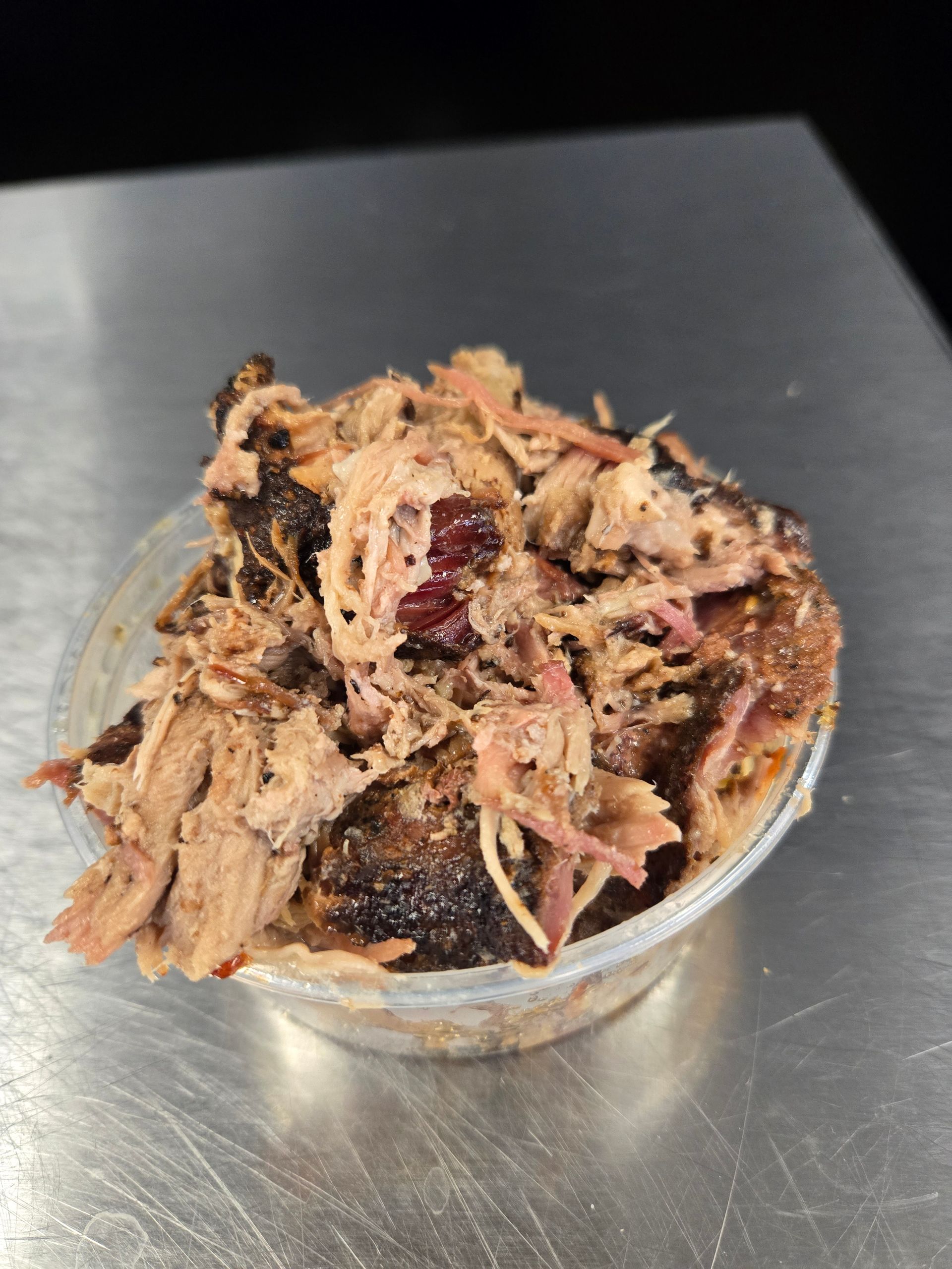 A small plastic container filled with pulled pork on a table.
