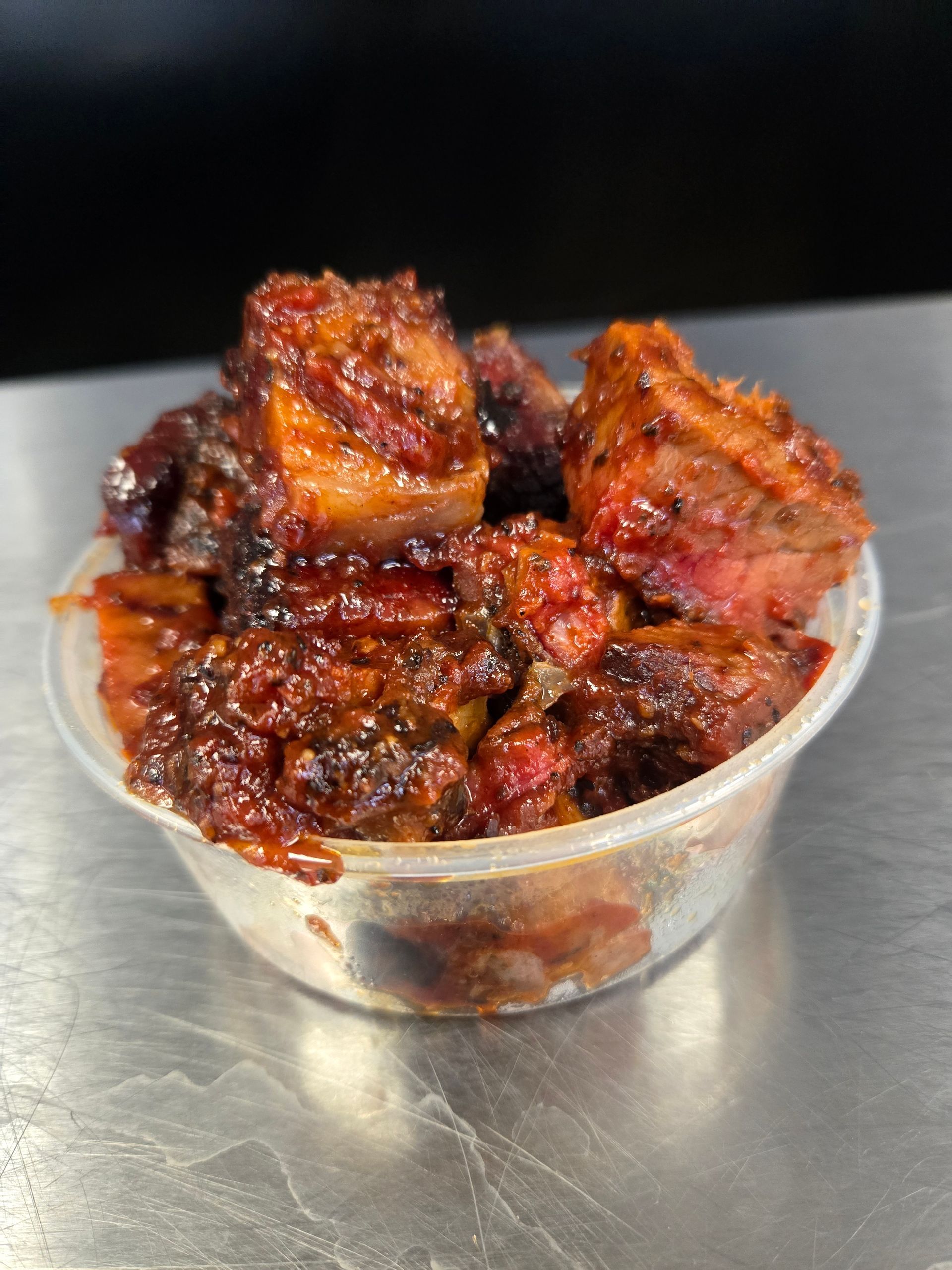 A plastic cup filled with meat and sauce is sitting on a table.