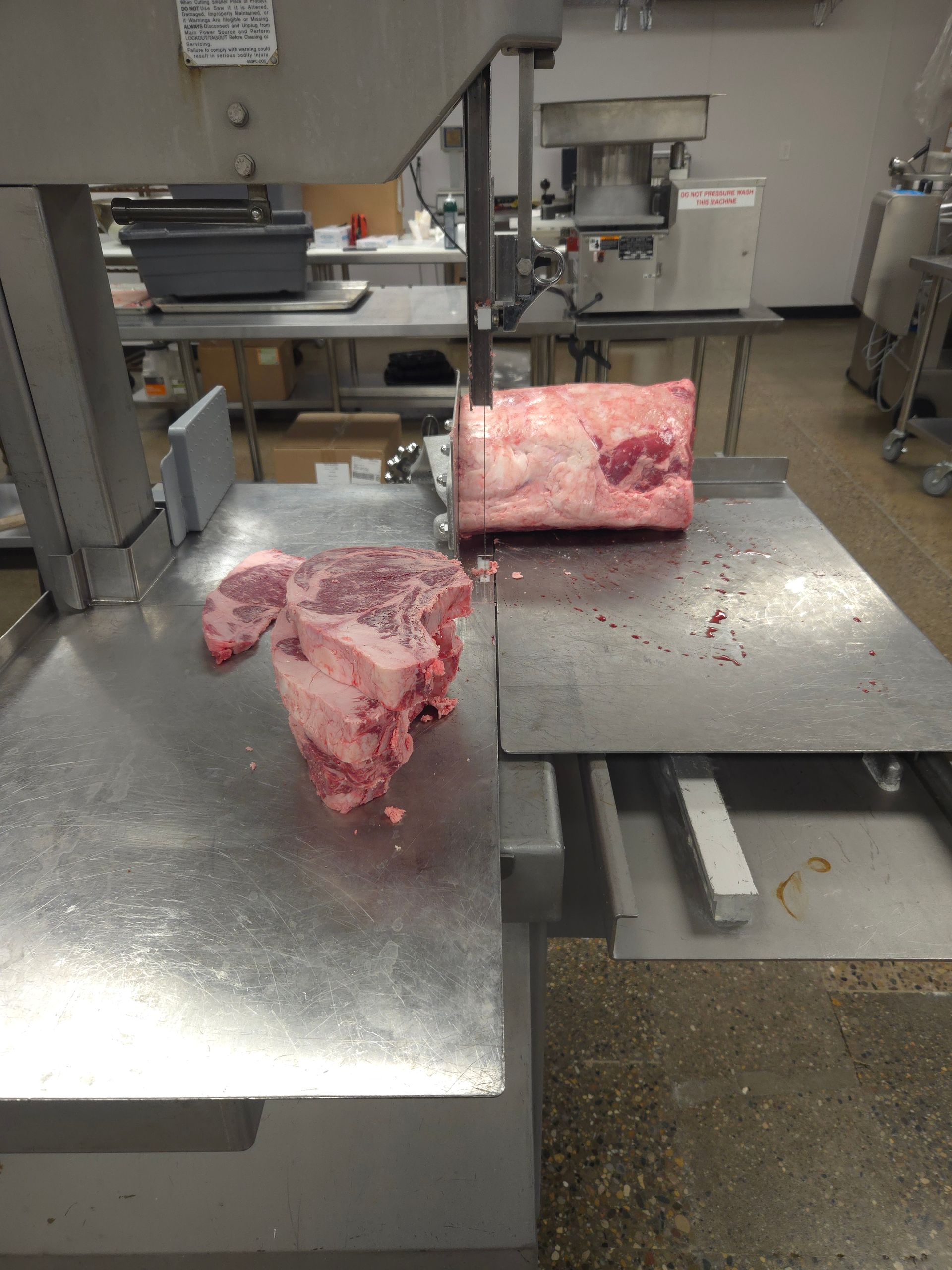 A large piece of meat is being cut on a band saw