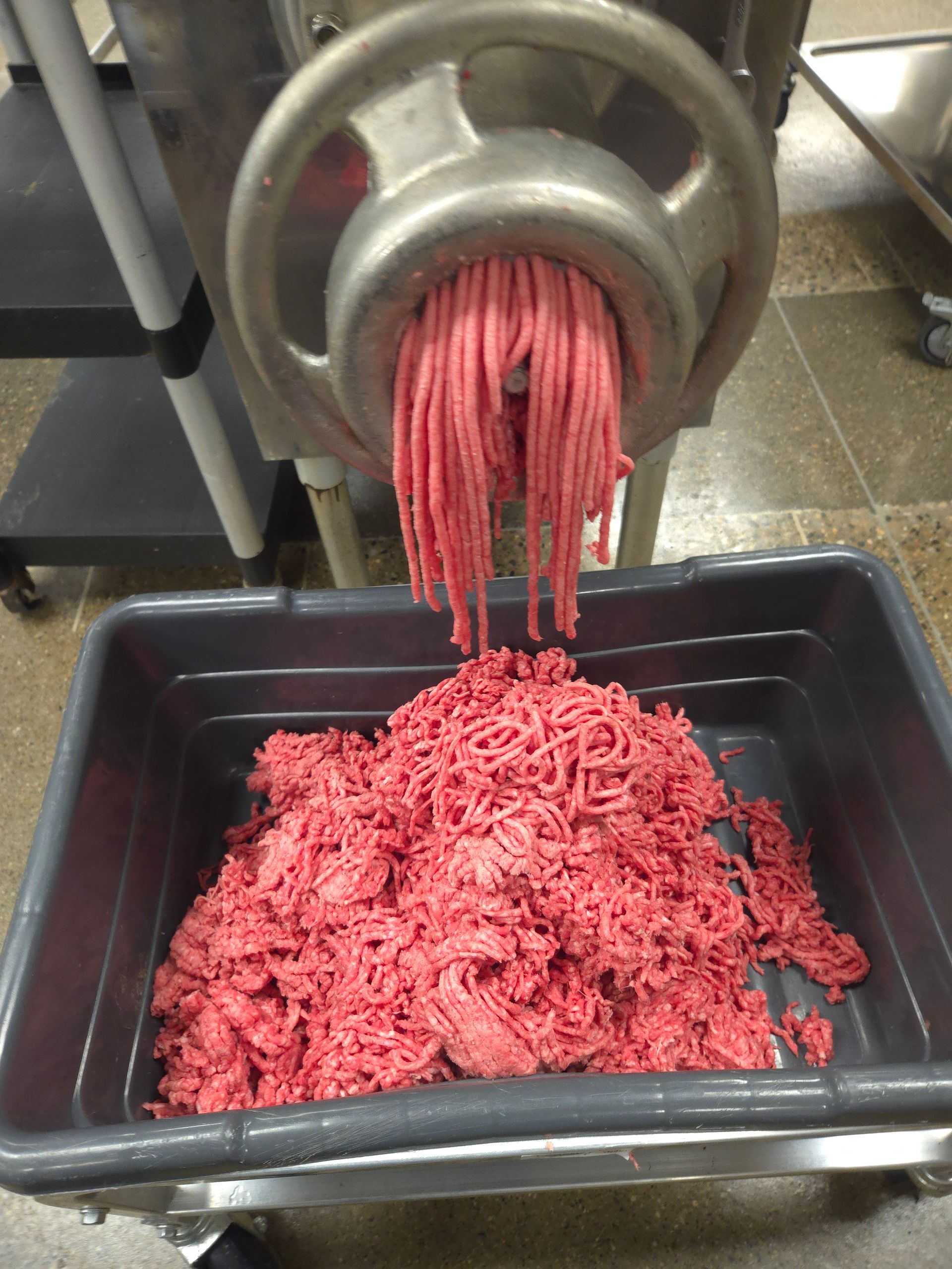 A tray of ground beef is being poured out of a meat grinder