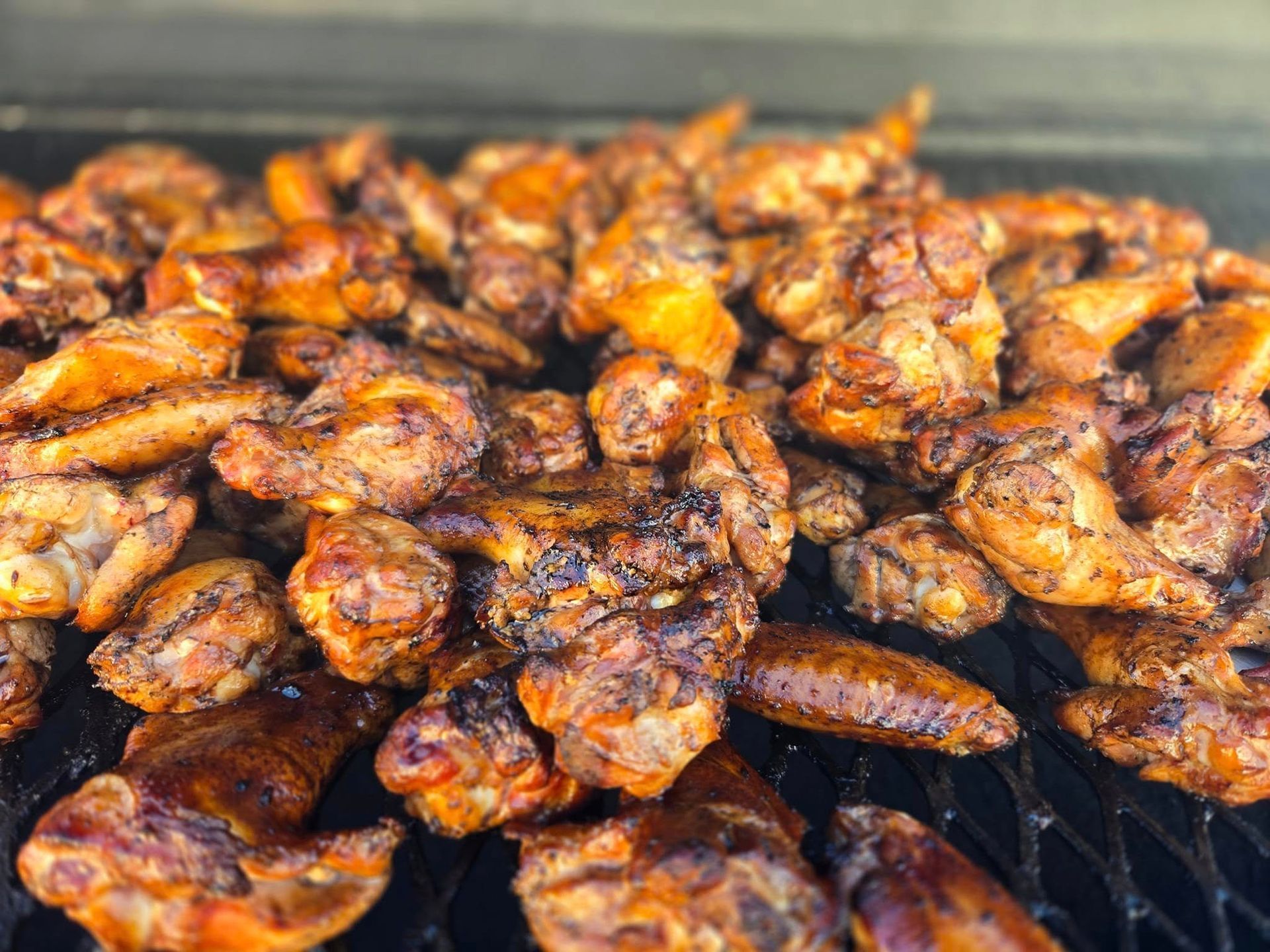 A pile of chicken wings cooking on a grill.
