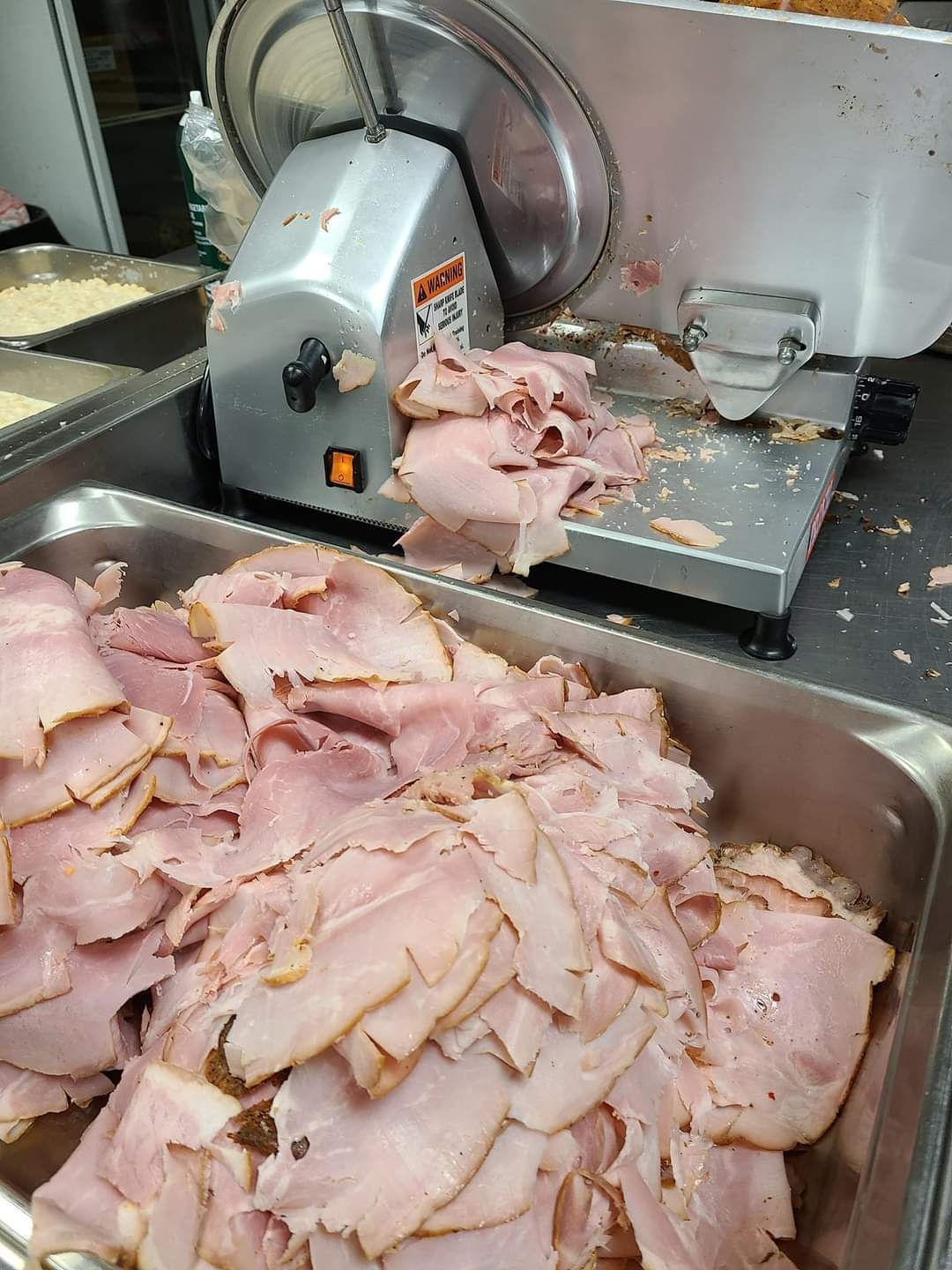 A tray of sliced ham is sitting next to a meat slicer.