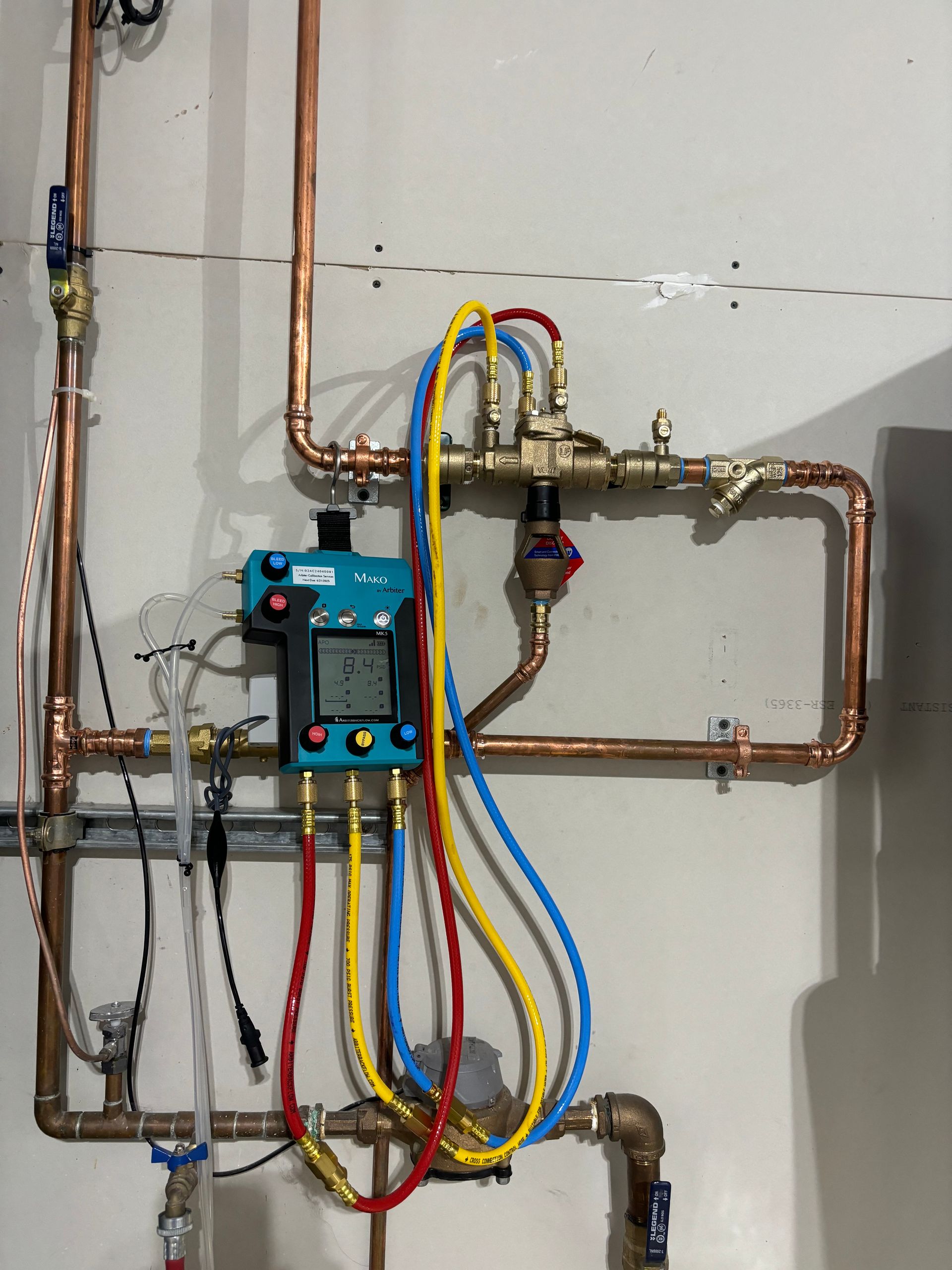 Blue control panel with copper pipes and colored hoses on a wall.