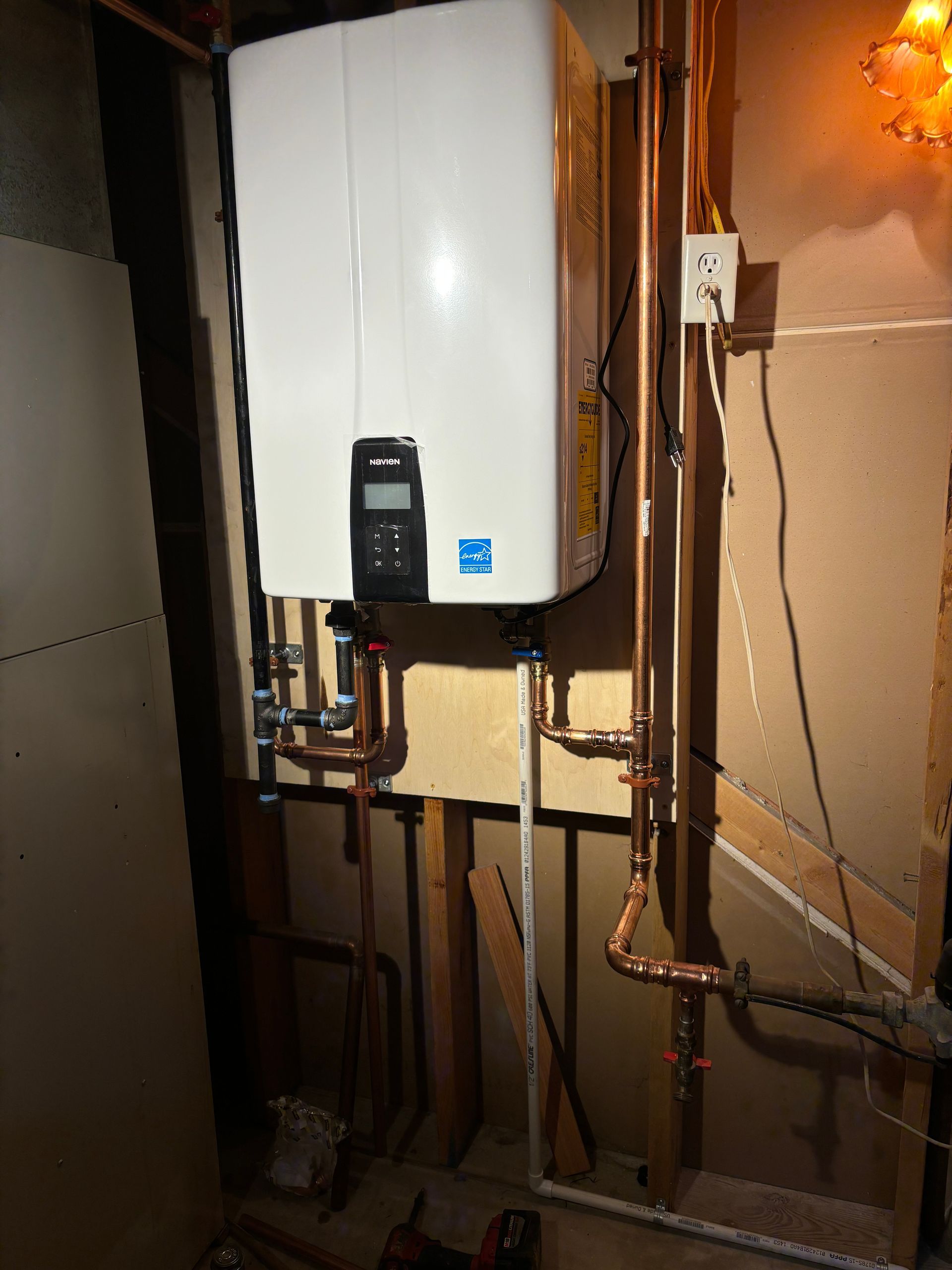 White water heater on wall with copper pipes.