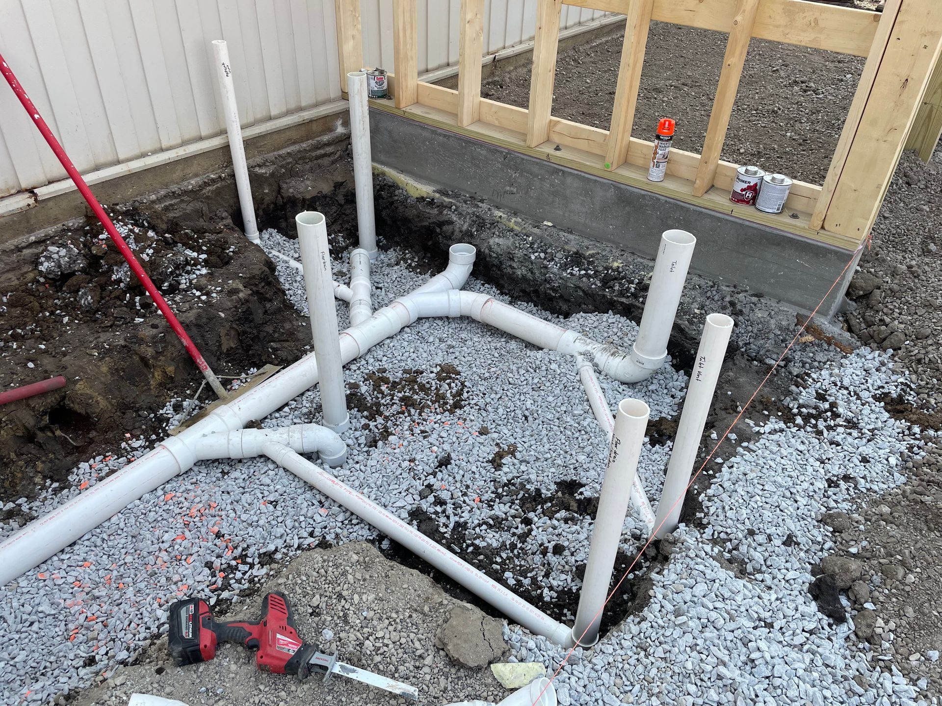 White PVC pipes, construction site, drainage and plumbing installation, gravel bed, wooden frame.