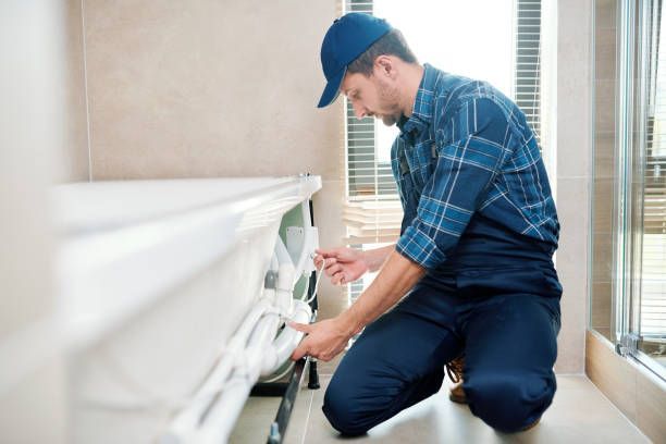Plumber in blue work clothes installing a white bathtub in a bathroom.