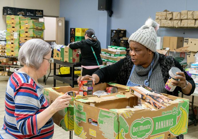 Two women are standing next to each other in front of boxes of food.