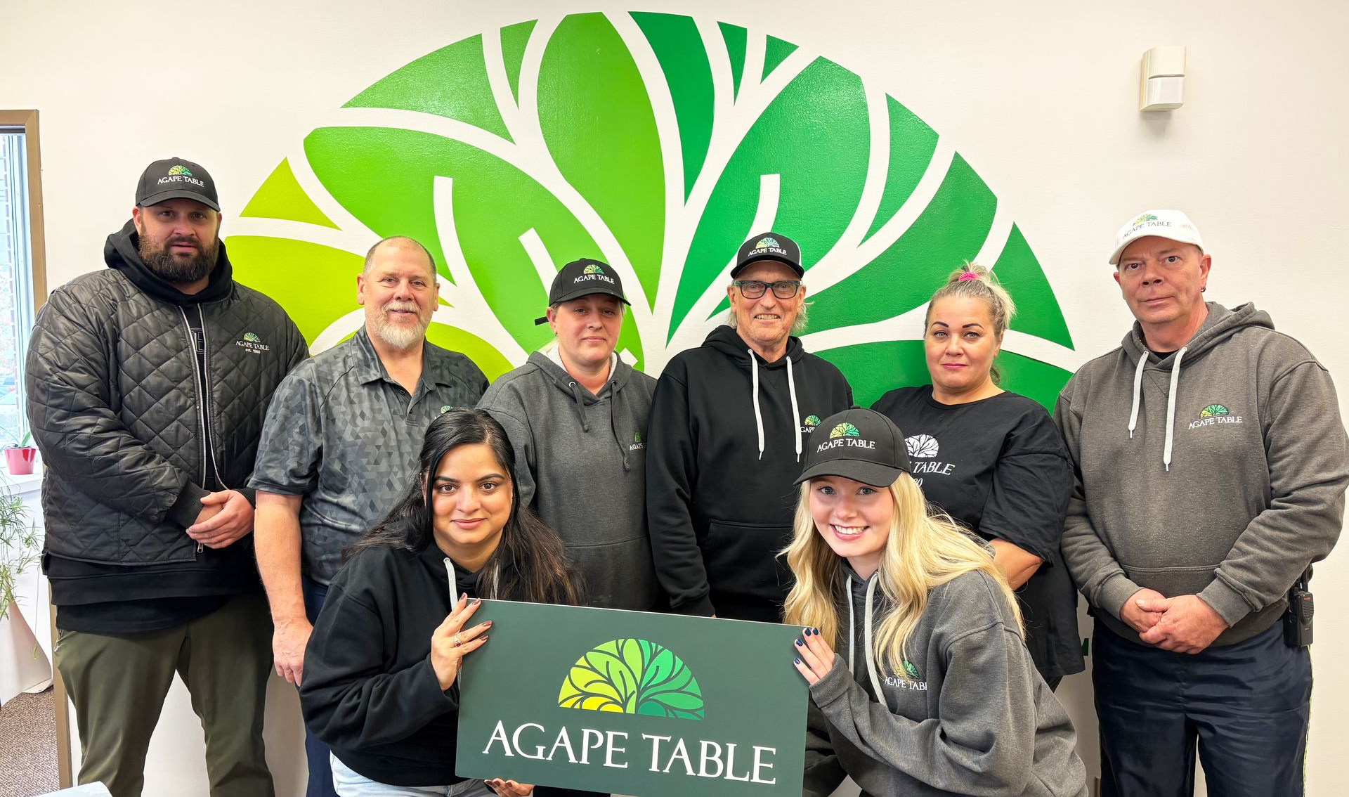 A group of people standing next to each other holding an Agape Table sign.