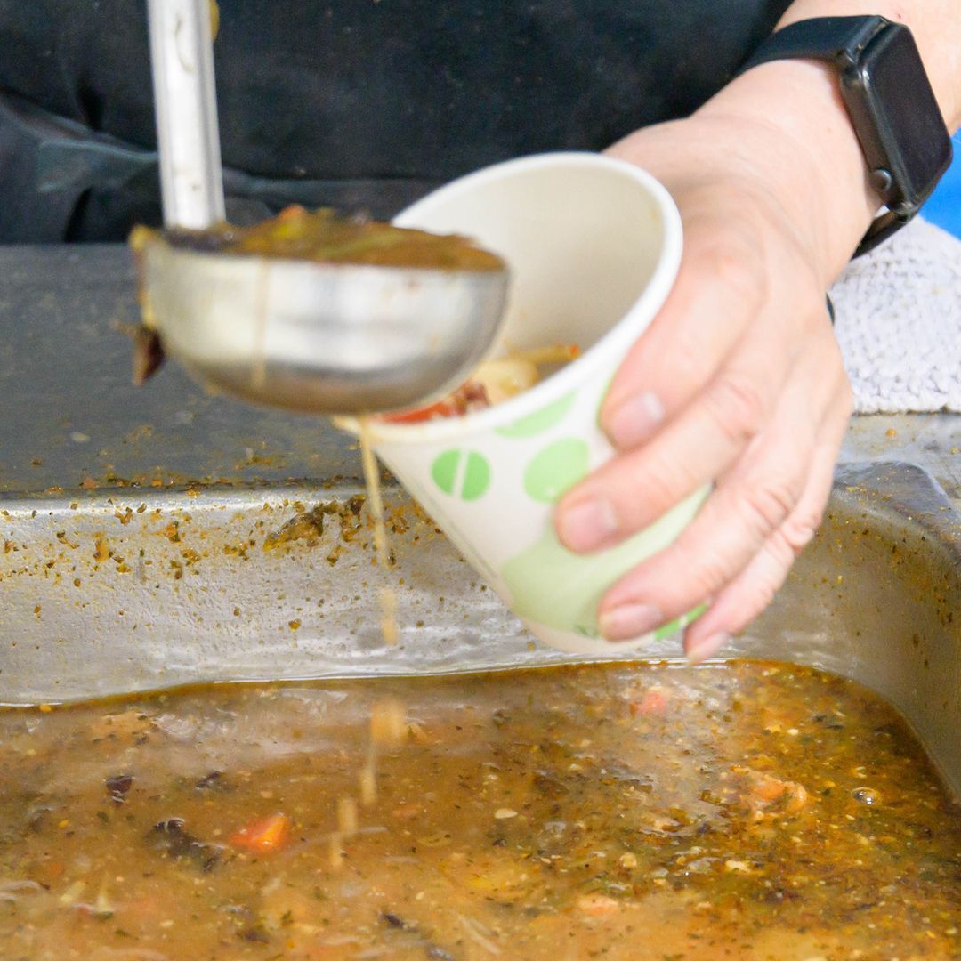 A person is pouring soup from a ladle into a cup