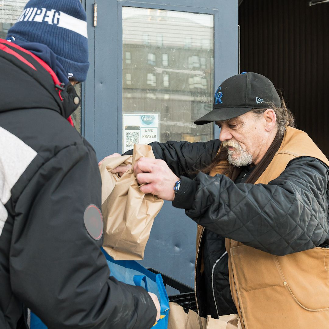 A man passing a bagged lunch to a person.