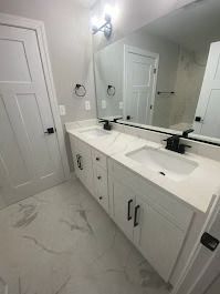 White bathroom with double vanity, black fixtures, and marble-look tile. Mirror reflects doors.