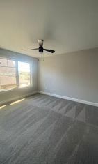 Empty bedroom with gray carpet, walls, and a ceiling fan near a window.