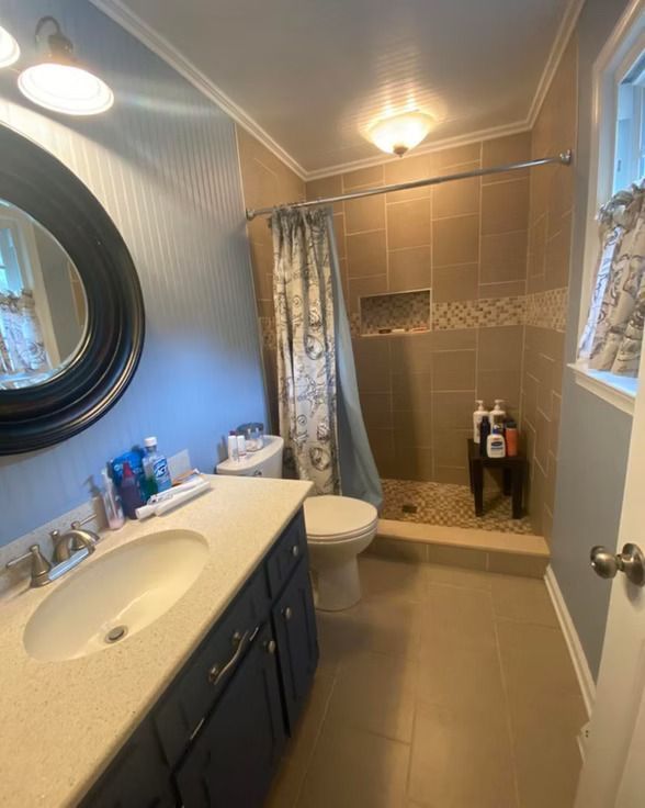 Bathroom with a blue vanity, toilet, and a tiled shower with a curtain.
