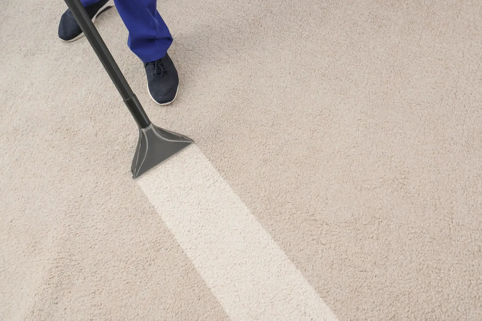 Person cleaning light-colored carpet with a vacuum, leaving a white path.