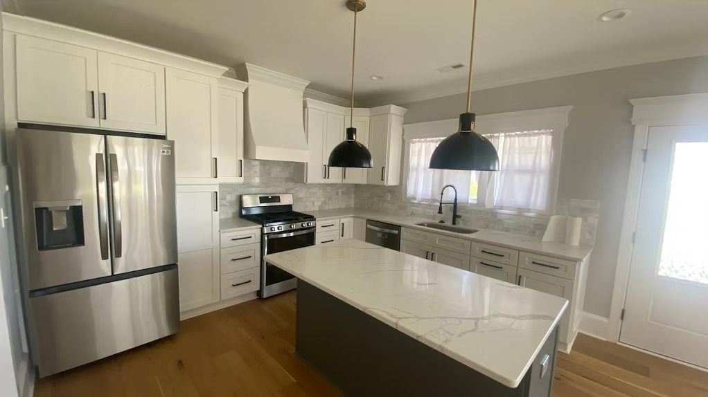 Modern kitchen with white cabinets, stainless steel appliances, and dark island. Two pendant lights hang over the island.