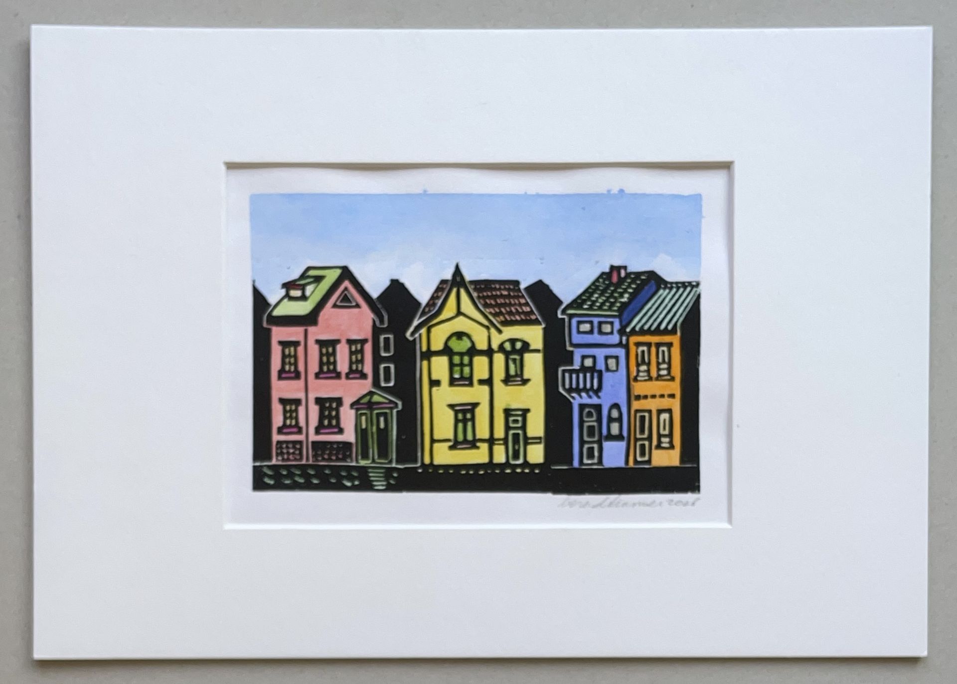 Een prent, ingelijst in wit, met vier kleurrijke, gestileerde huizen op een rij tegen een lichtblauwe lucht.