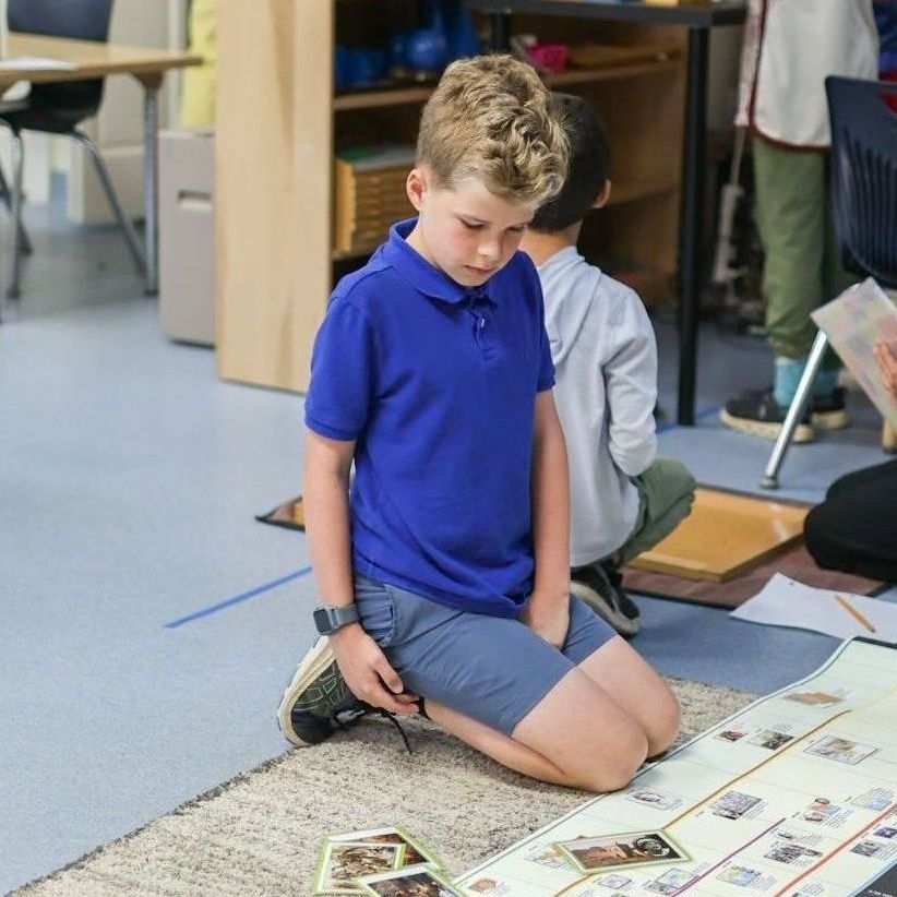 A boy in a blue shirt is kneeling on the floor reading a book