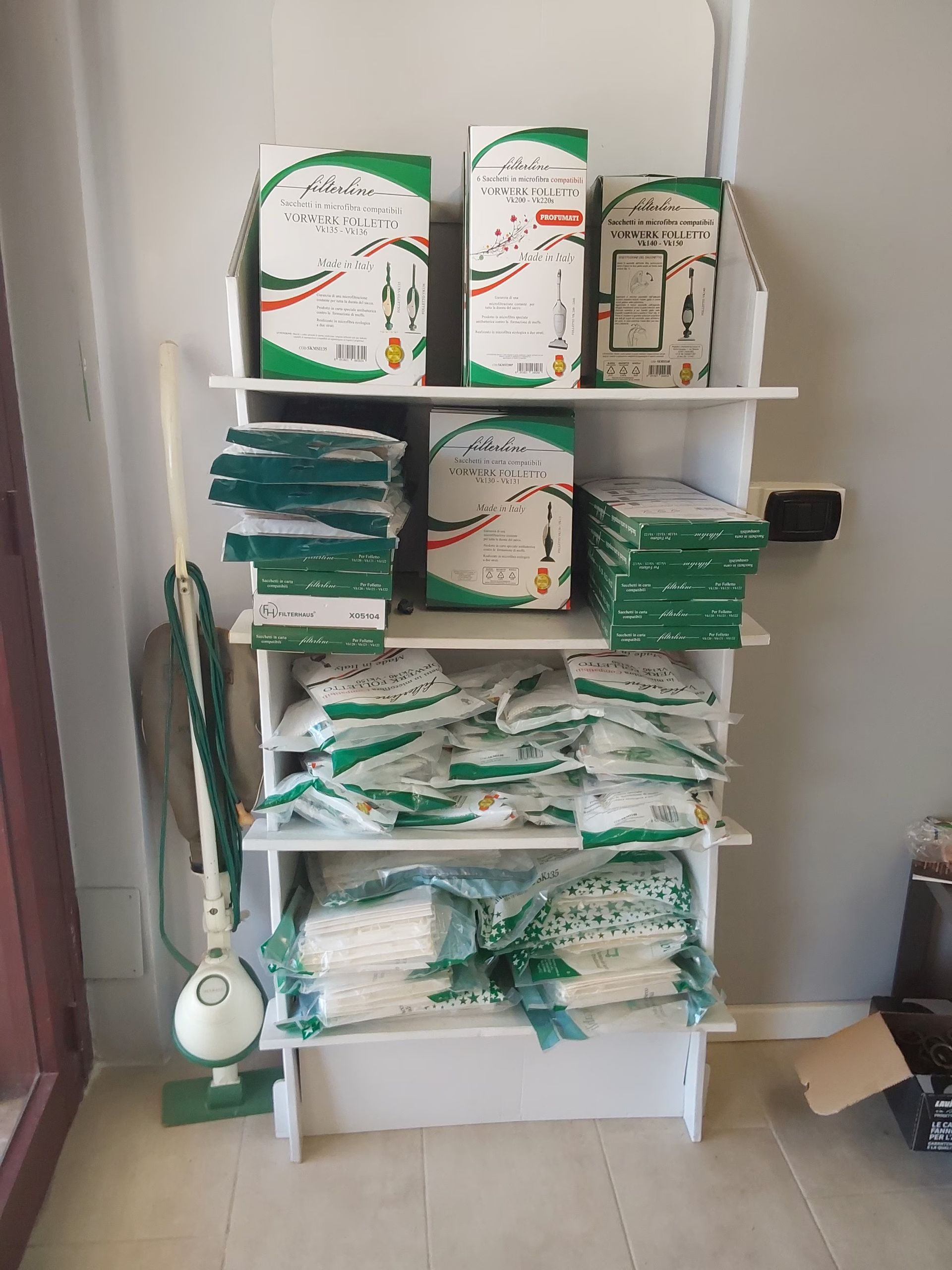 Un aspirapolvere è appoggiato su uno scaffale pieno di scatole e sacchetti.