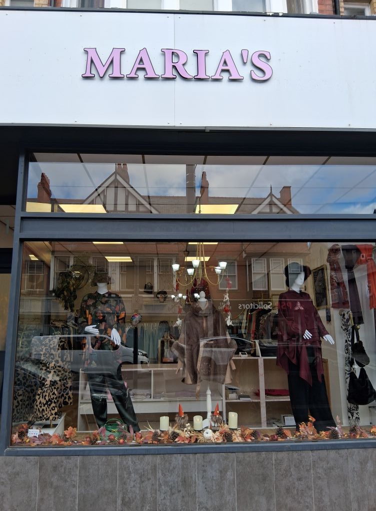 Maria's shopfront with pink sign, window display of clothing, mannequins, fall decor, and street reflection.