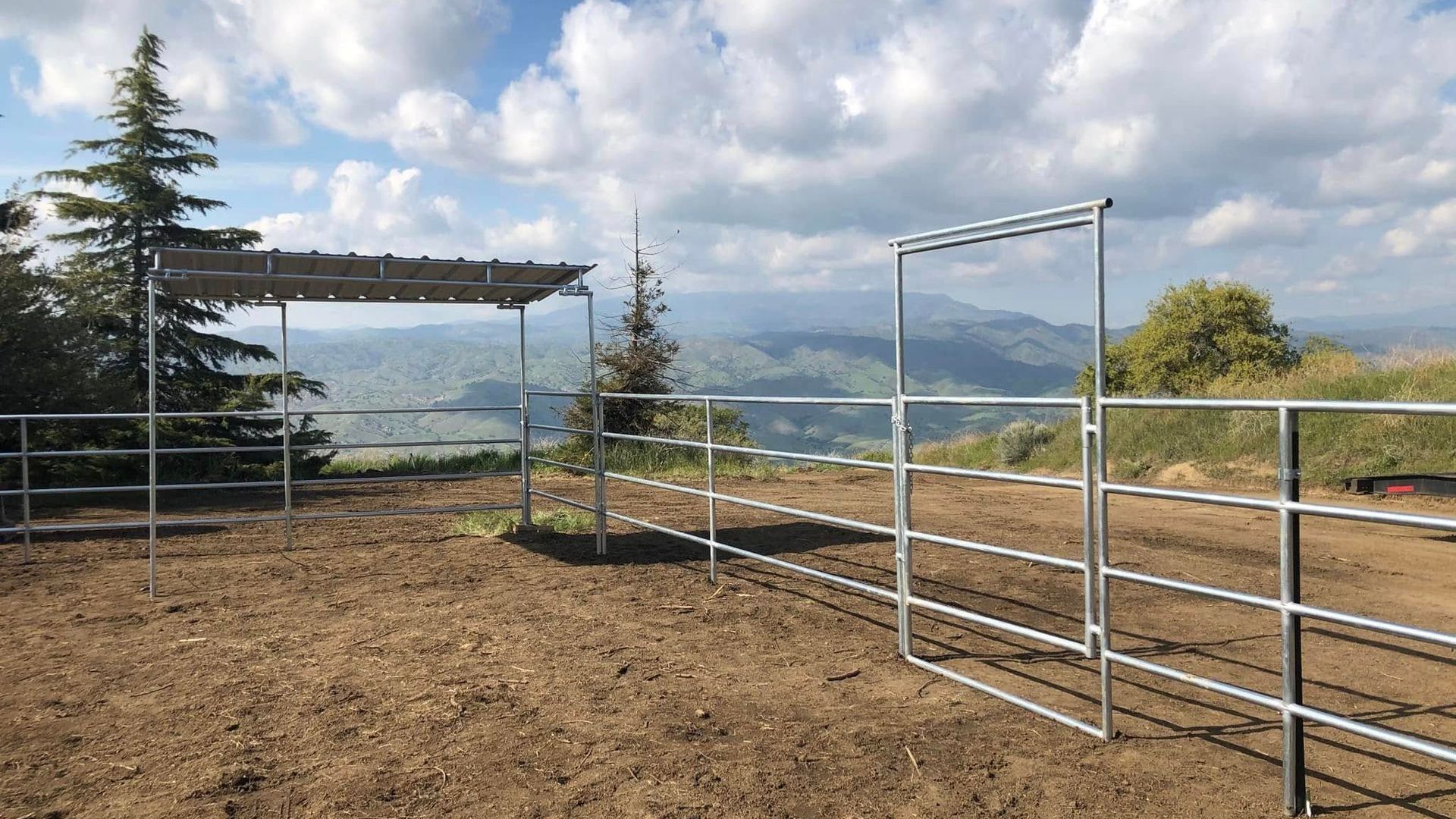 A metal fence surrounds a dirt field with mountains in the background.