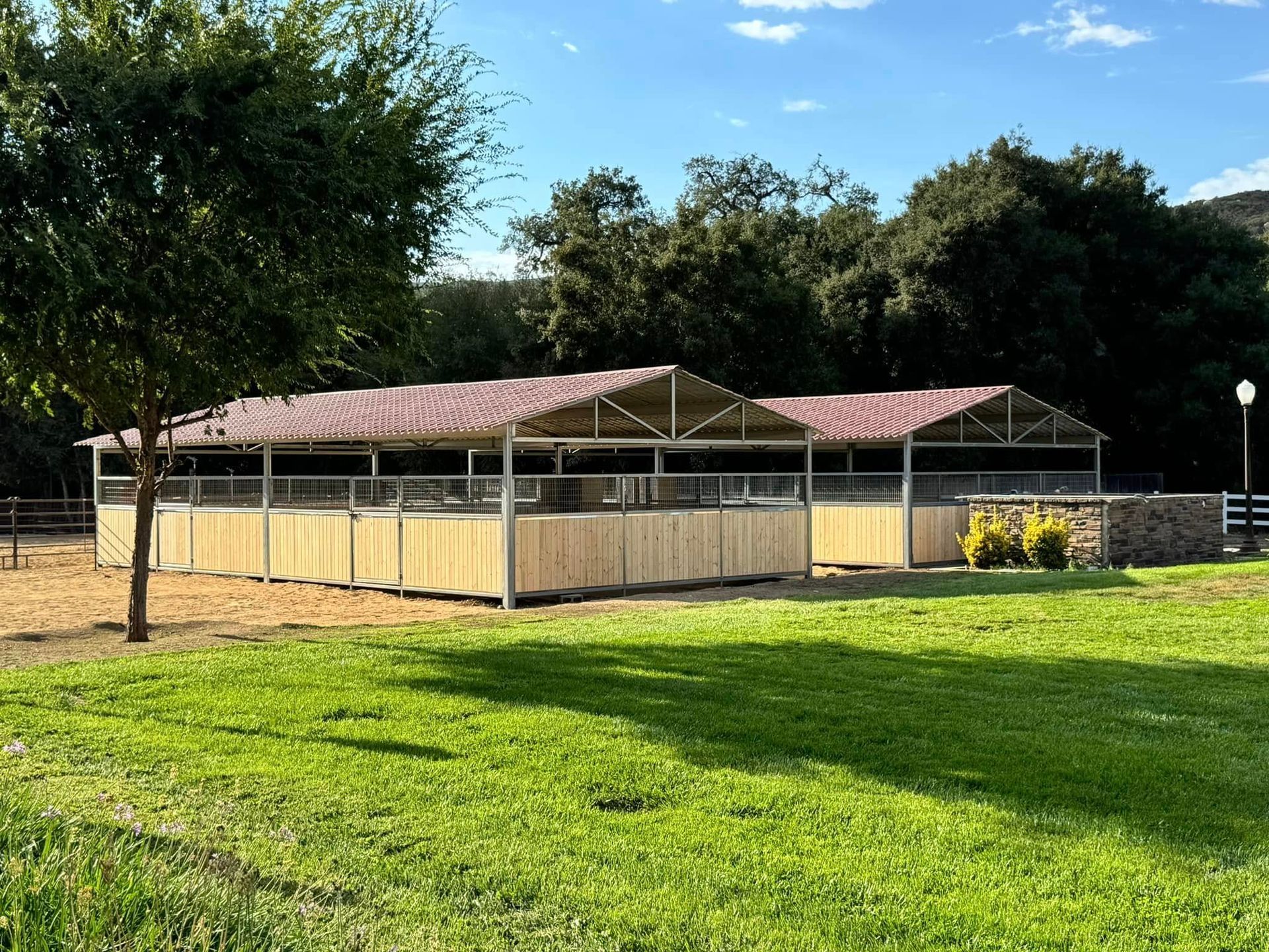 A row of horse stables in a grassy field with trees in the background.