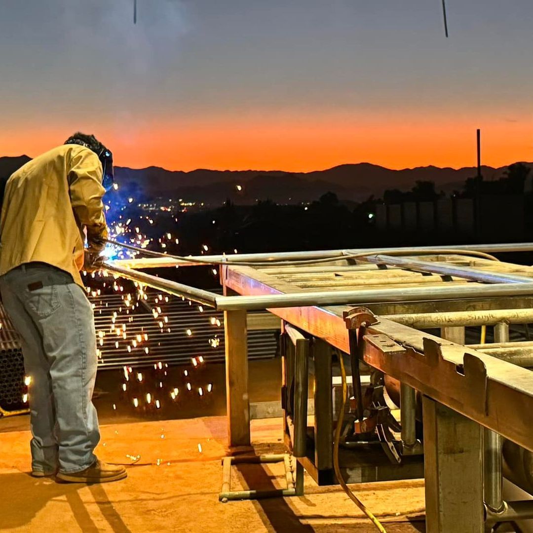 A man is welding a metal structure with a sunset in the background