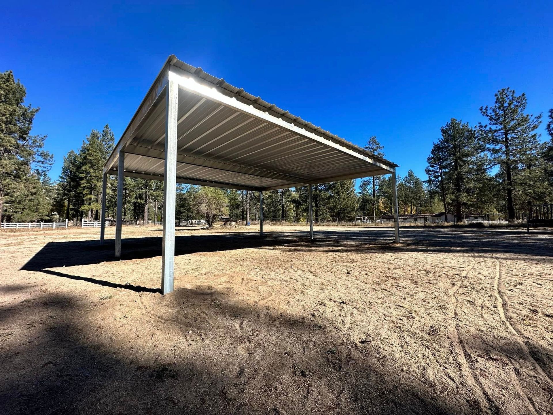 A carport is sitting in the middle of a dirt field surrounded by trees.