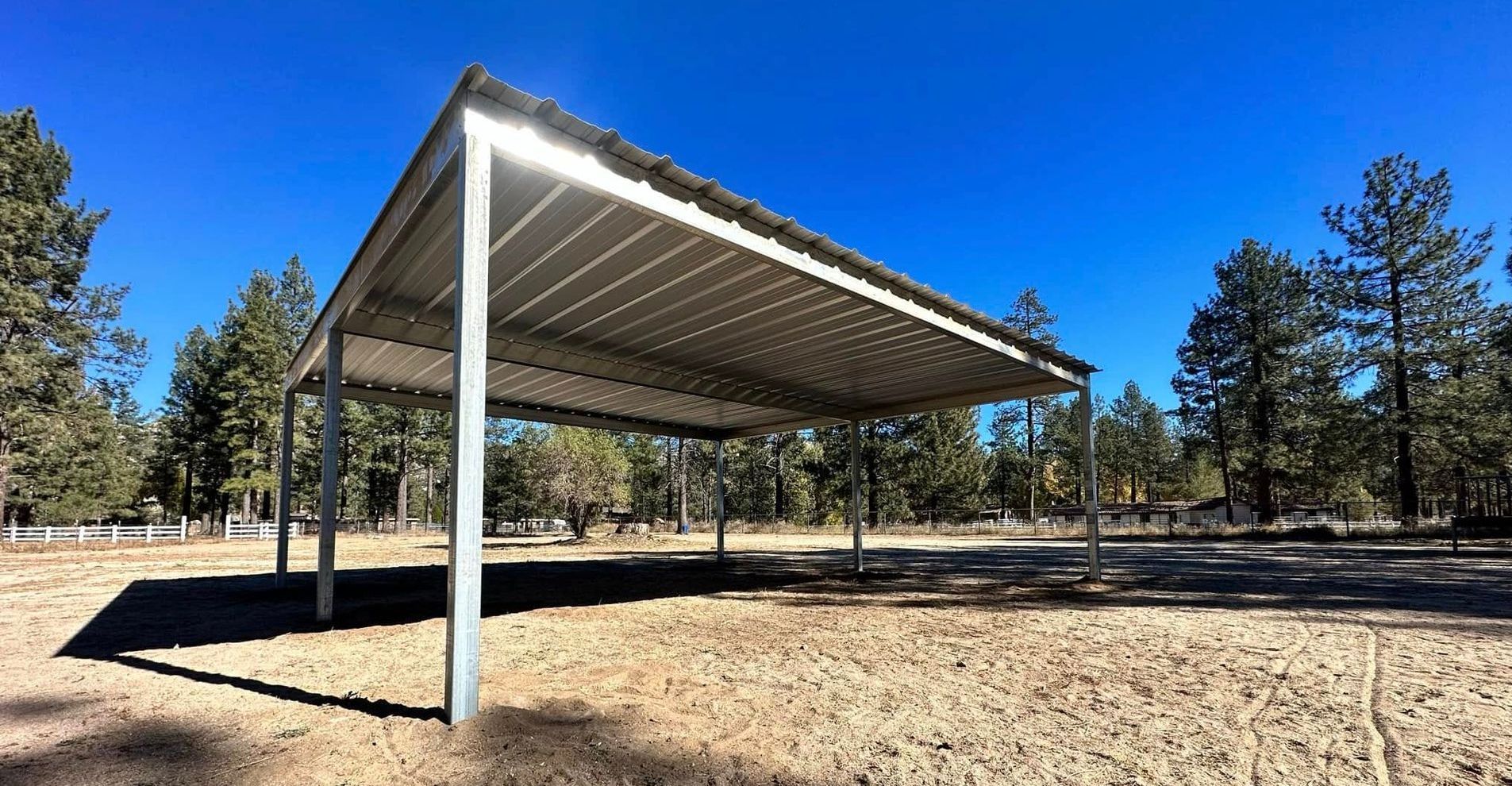 A carport is sitting in the middle of a dirt field next to a fence.