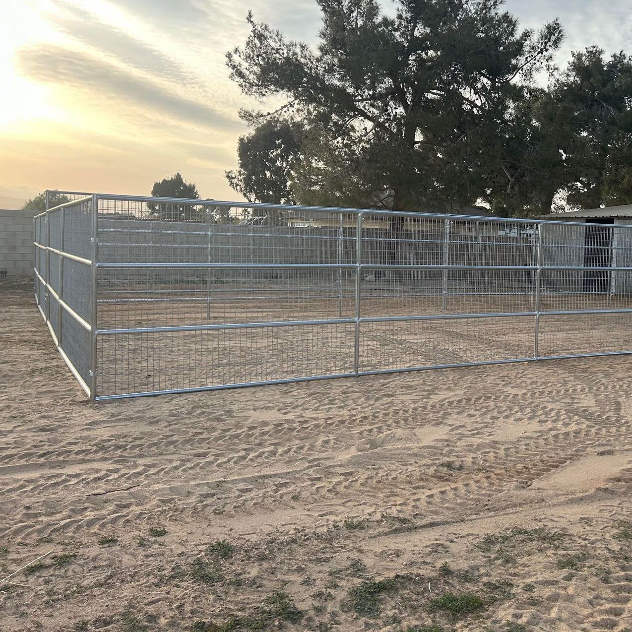 A metal fence surrounds a dirt field with trees in the background.