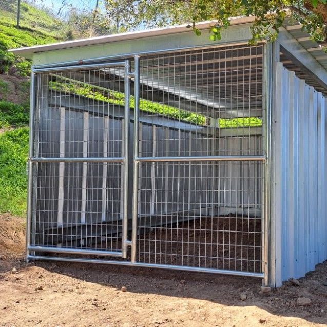 A dog kennel is sitting in the dirt next to a tree.