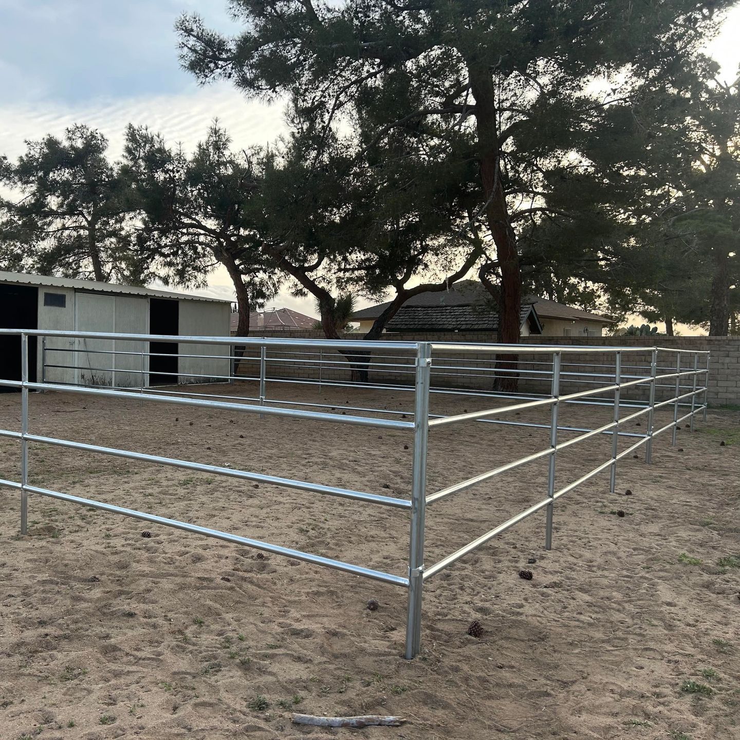 A metal fence surrounds a dirt field with trees in the background.