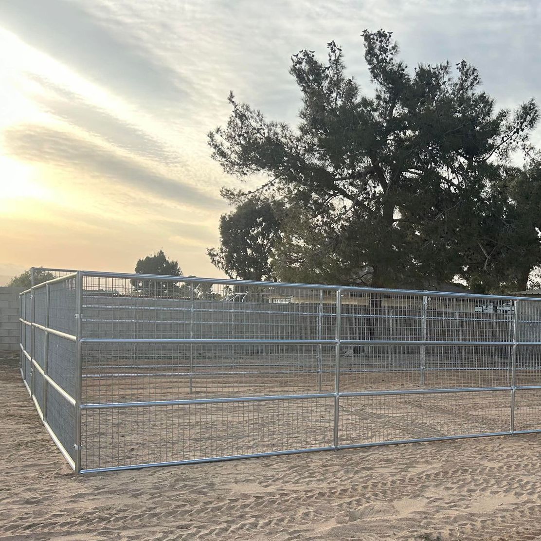 A metal fence surrounds a dirt field with trees in the background.