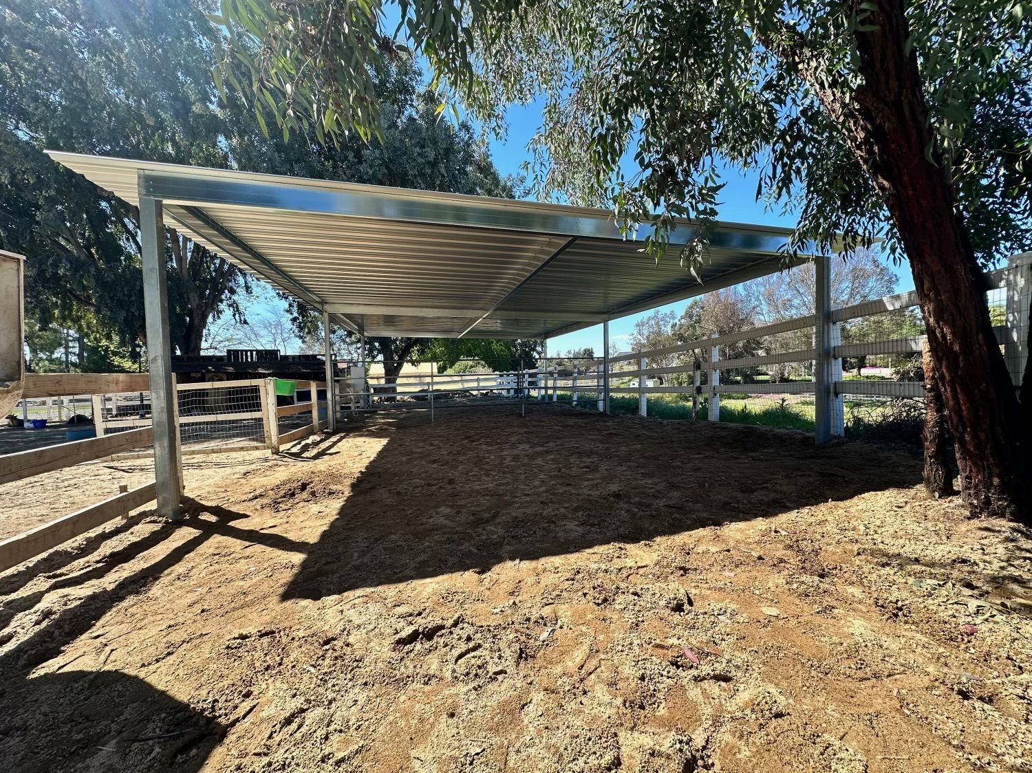 A carport is sitting in the middle of a dirt field next to a fence.