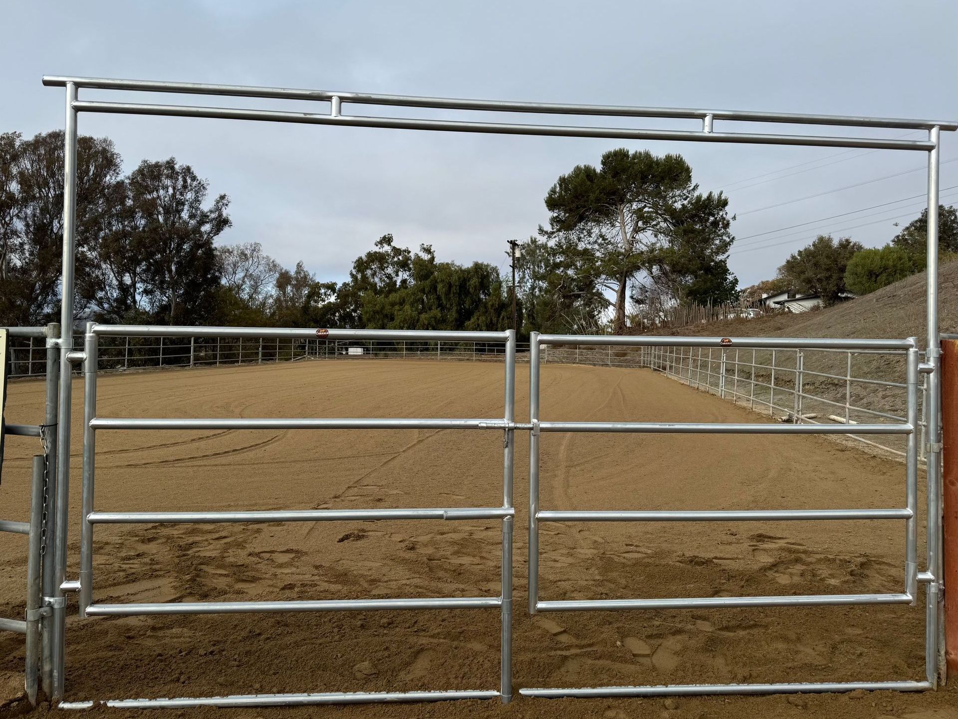 A metal fence surrounds a dirt field with trees in the background