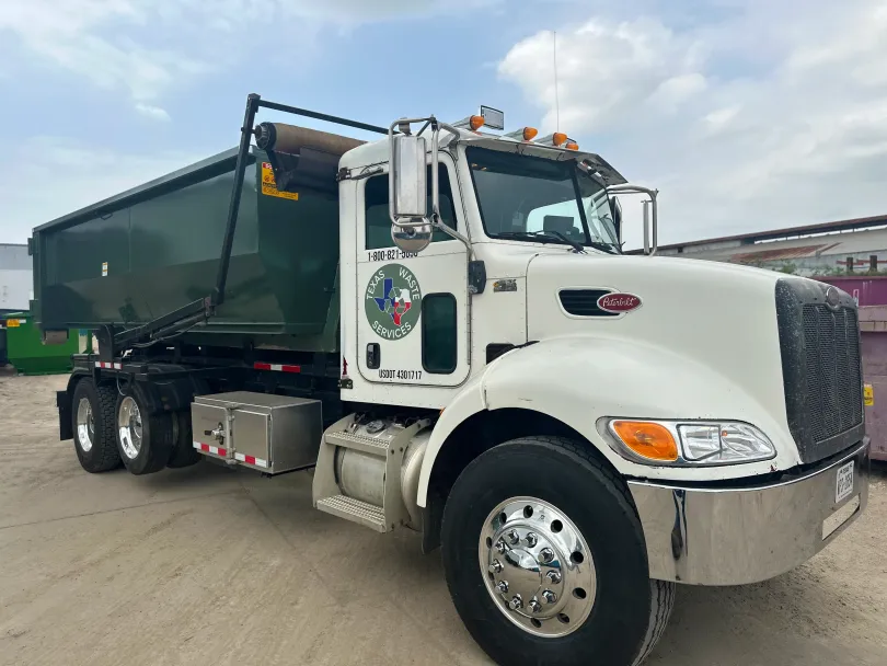 A dump truck with a green dumpster attached to it is parked in a parking lot.